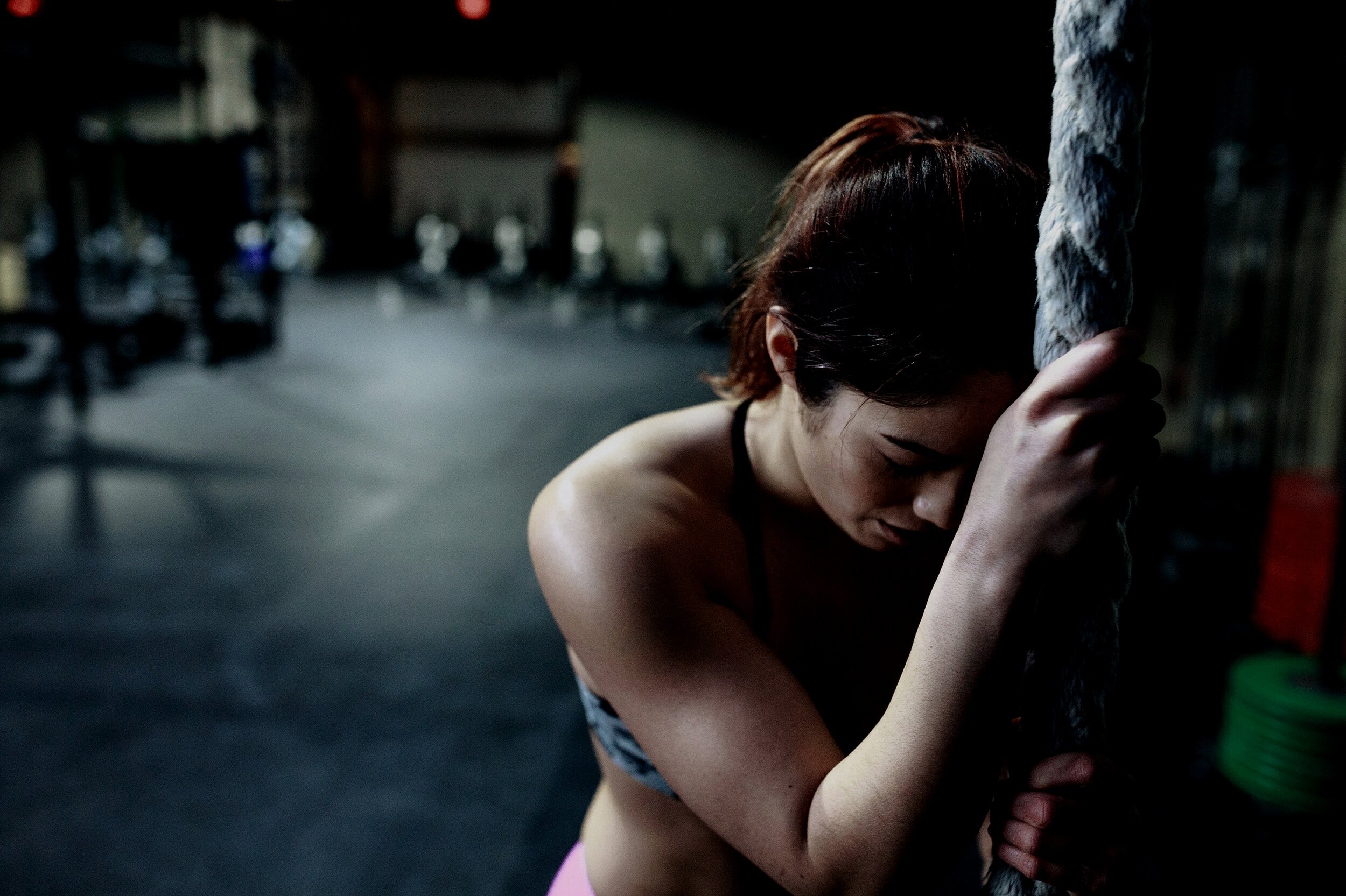 Athlete resting against a heavy climbing rope in a dark gym