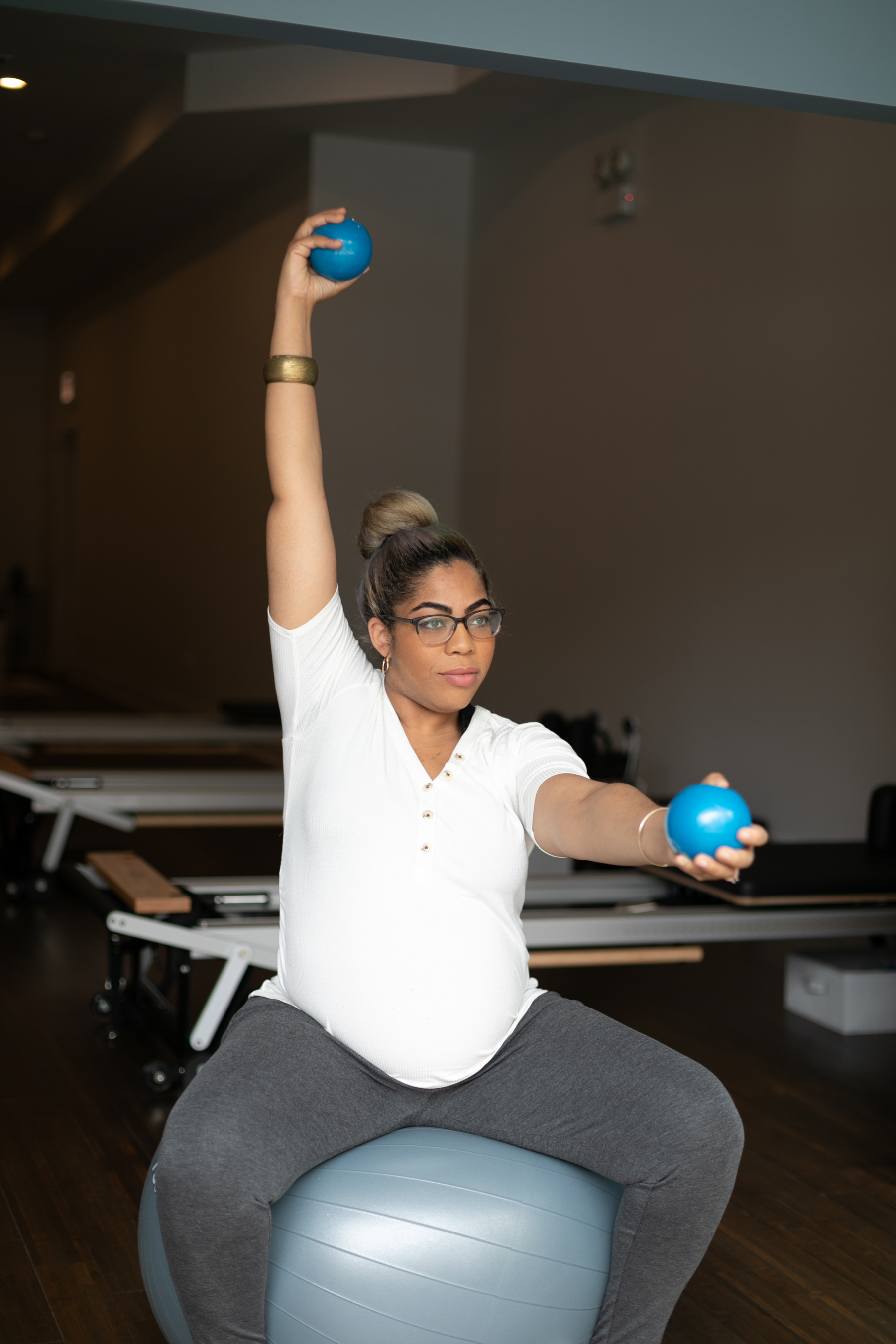 A pregnant client on an exercise ball with reformers behind her at Restore Pilates