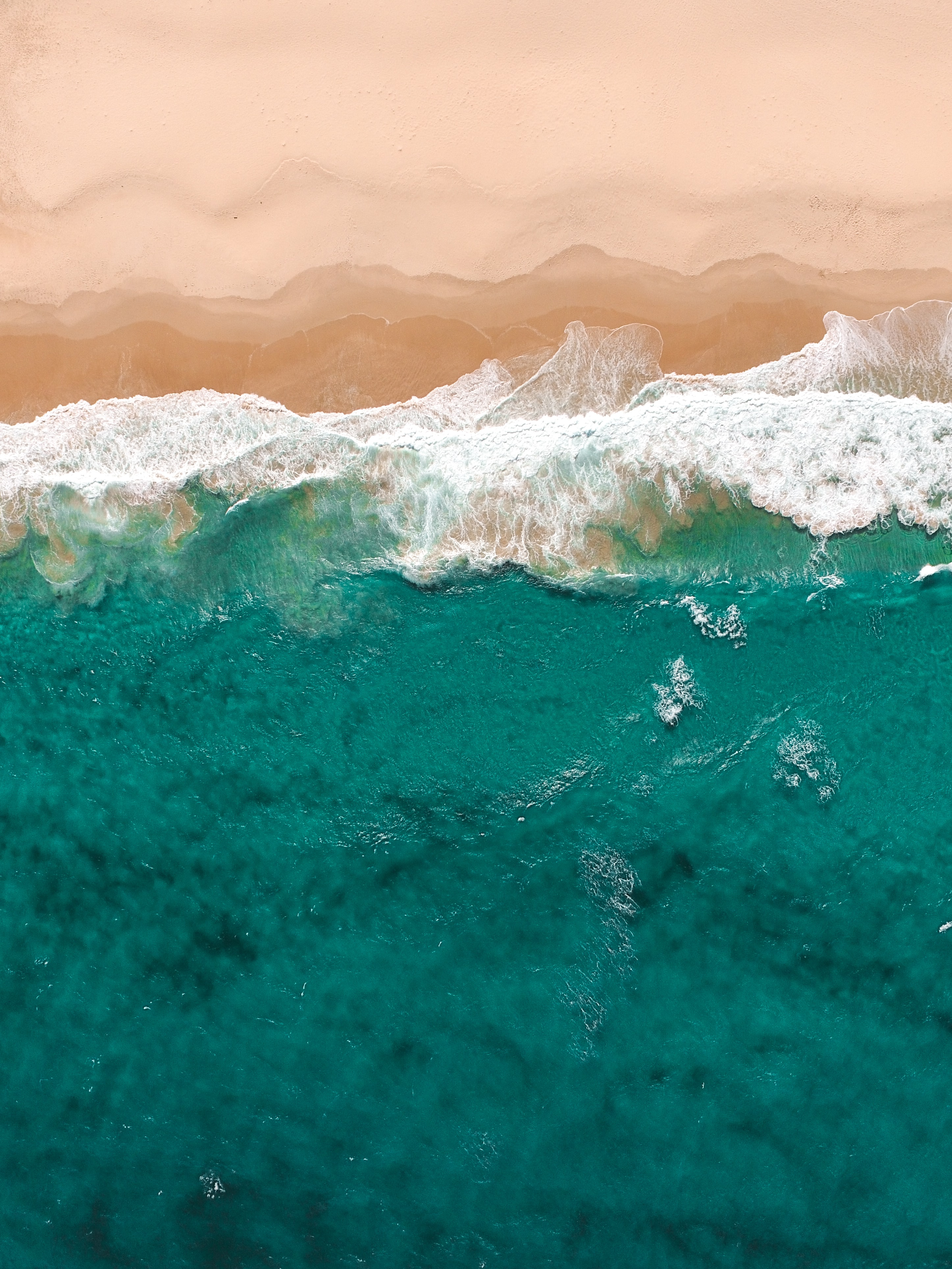 Aerial view of turquoise ocean waves meeting sandy beach