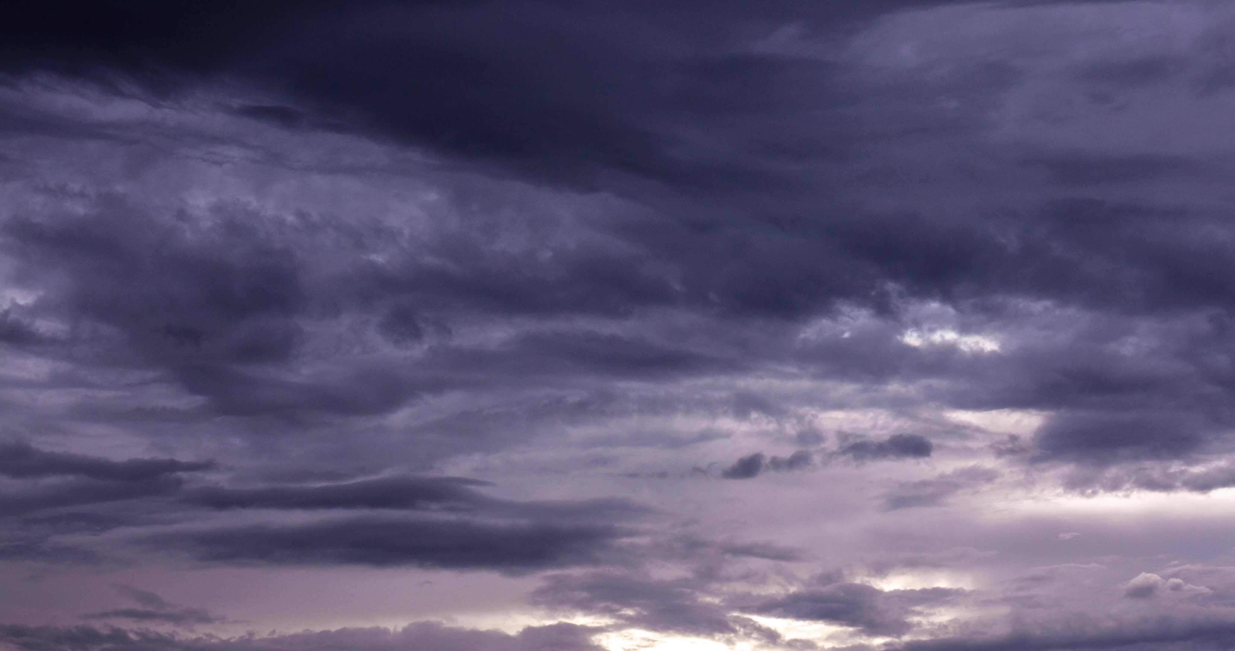 Dramatic stormy sky with heavy purple-grey clouds and a luminous break of light near the horizon