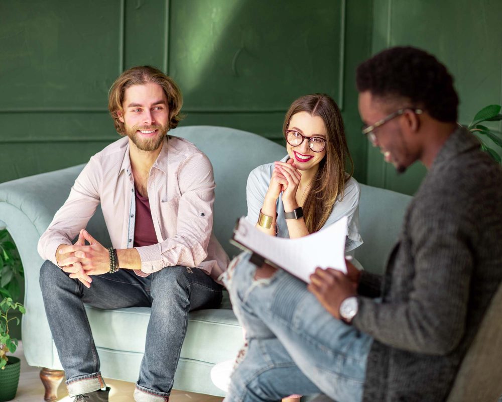 A young couple meeting with a coach on a teal couch