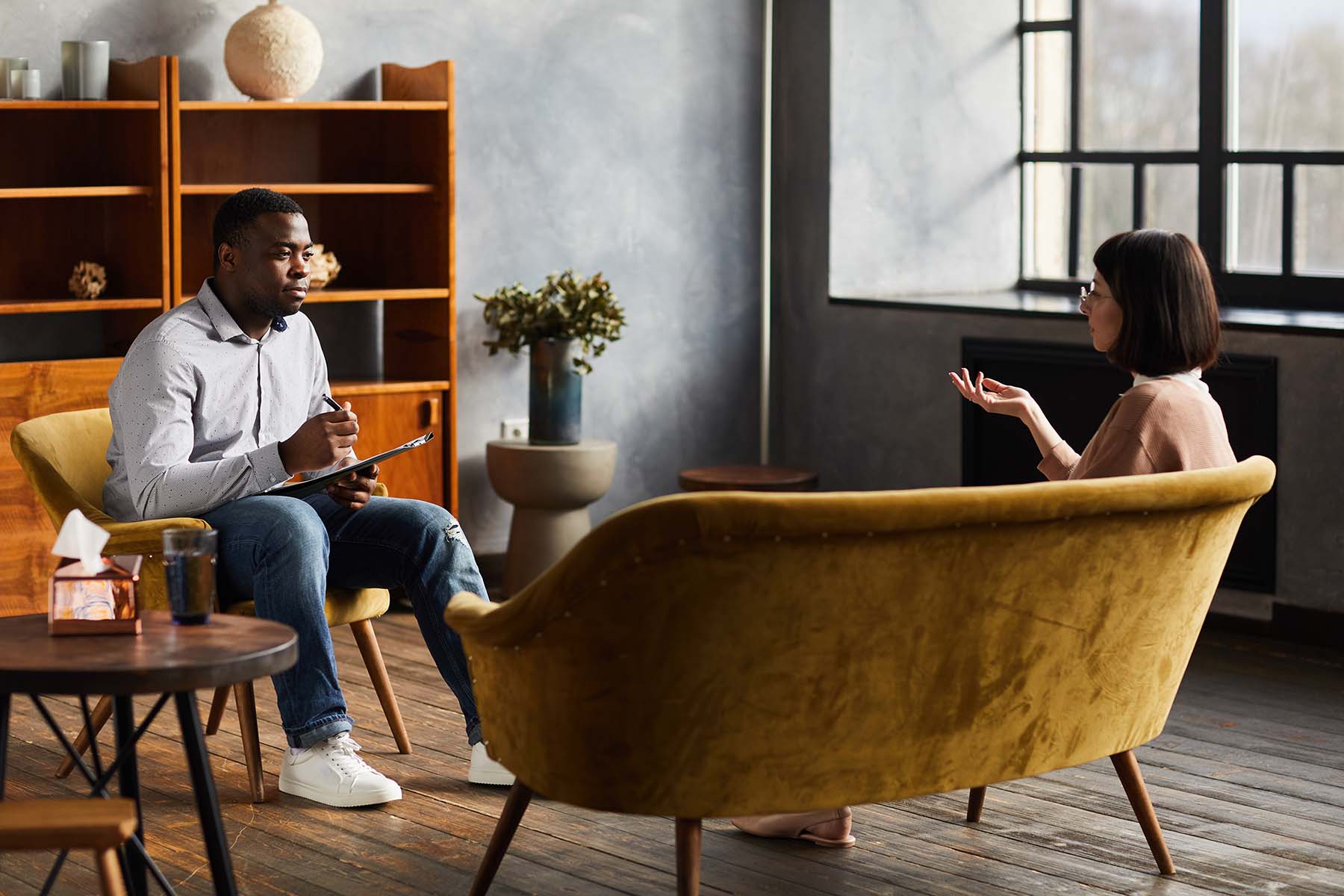 A coach and client in conversation in a warm, modern office with yellow armchairs
