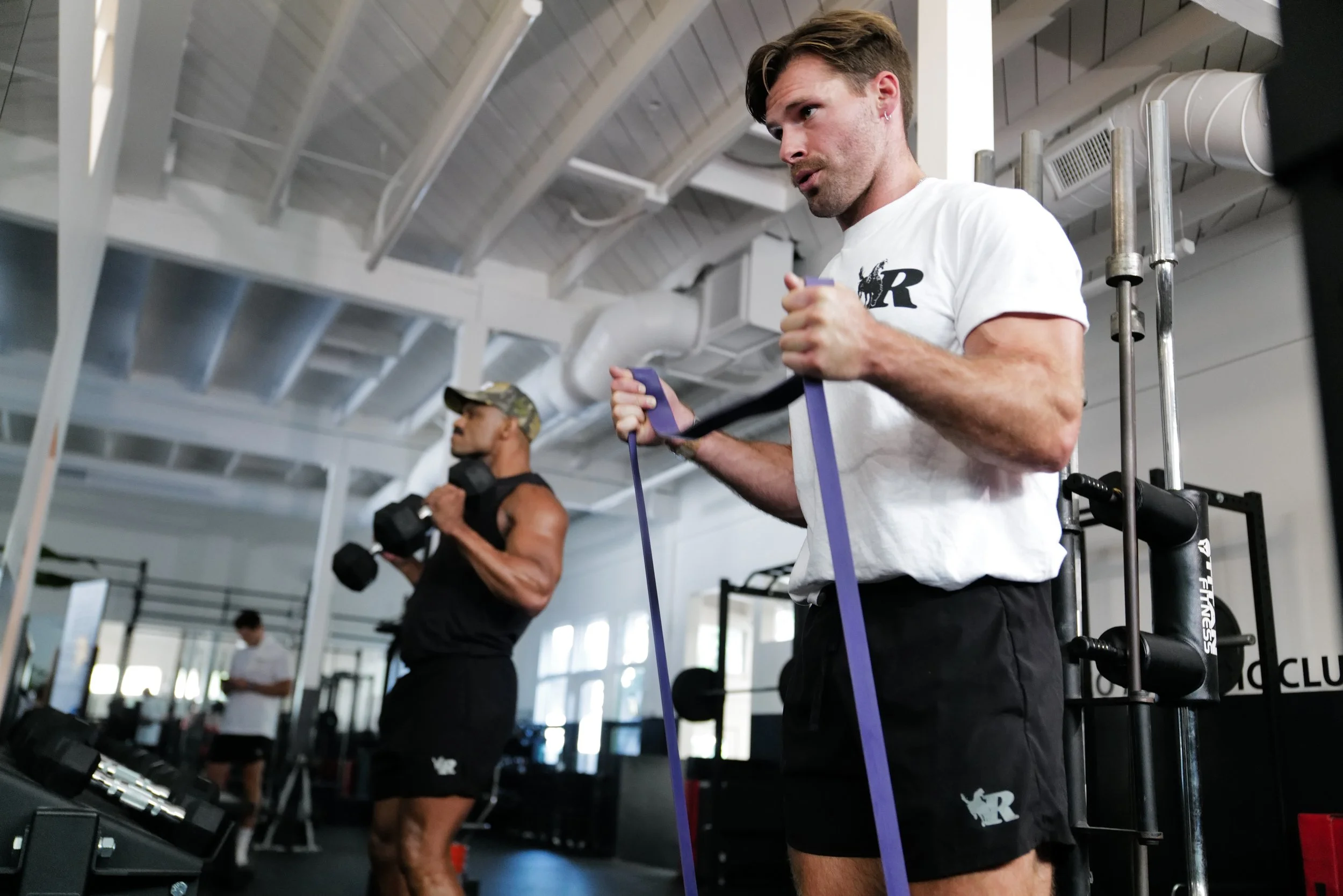 Two members training with a resistance band and dumbbells in Rodeo Athletic Club apparel