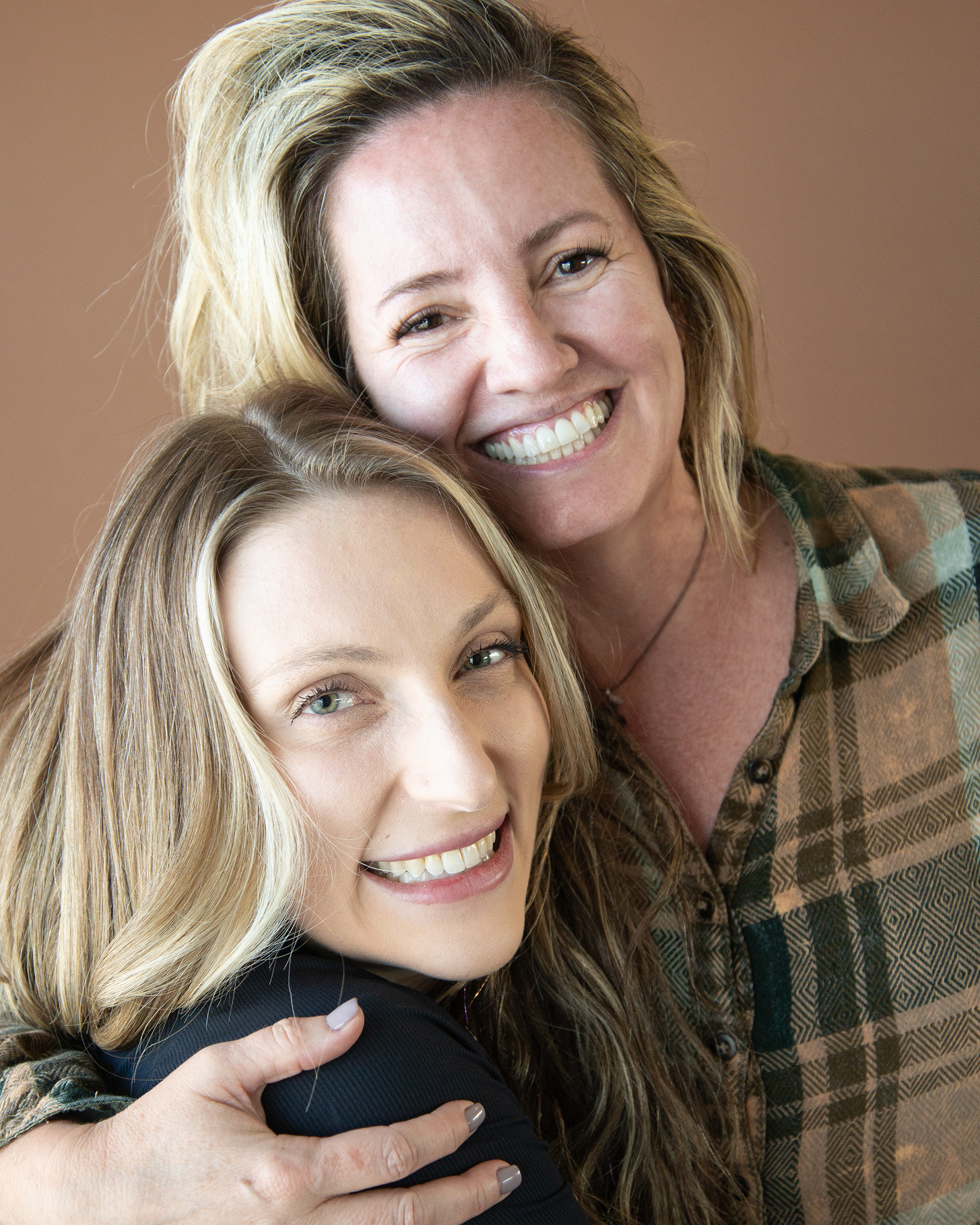 Andi and Jessie, the owners of Root to Rise, smiling cheek to cheek in a studio portrait