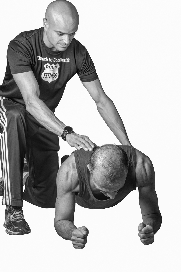 Route Fitness trainer spotting a client during a plank exercise