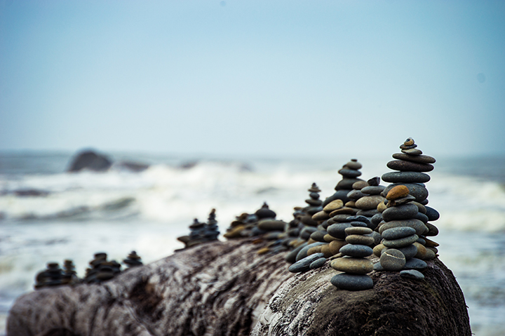 Stacked stone cairns balanced on driftwood beside the ocean