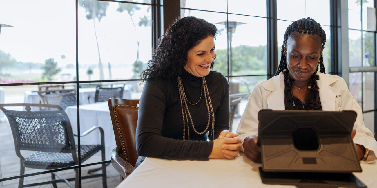 Two women reviewing content on a tablet at a table by large windows