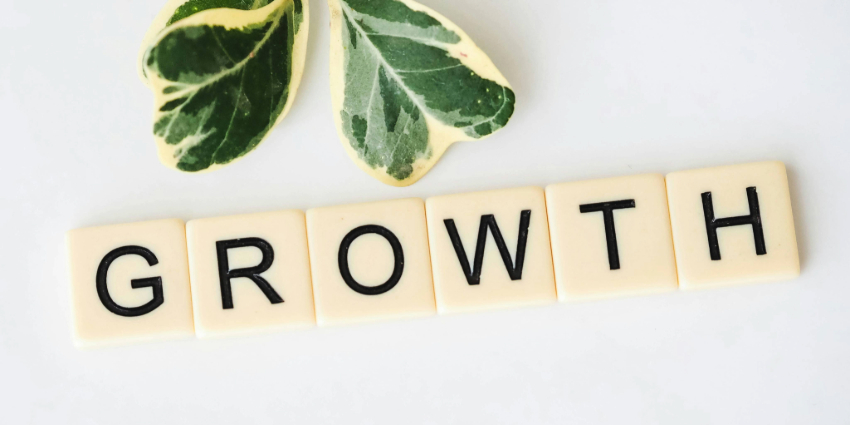 Scrabble tiles spelling GROWTH beside a small plant