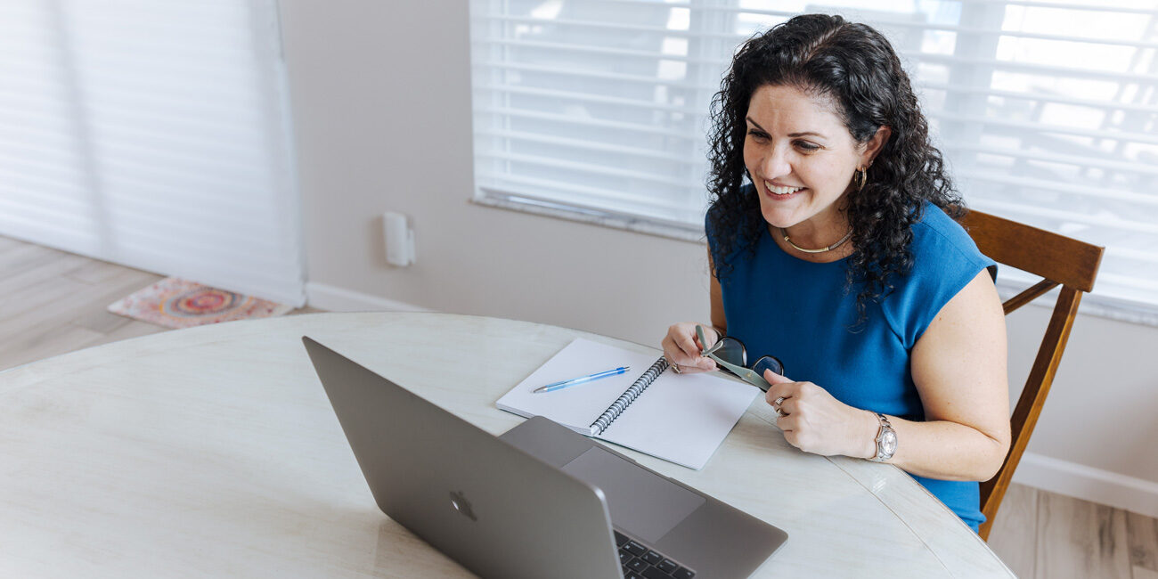 Stacy Berg Jackson in a blue top smiling at a laptop in a bright home office