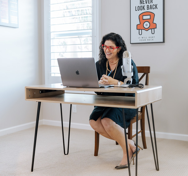 Stacy Berg Jackson smiling at a laptop at a modern desk with a microphone