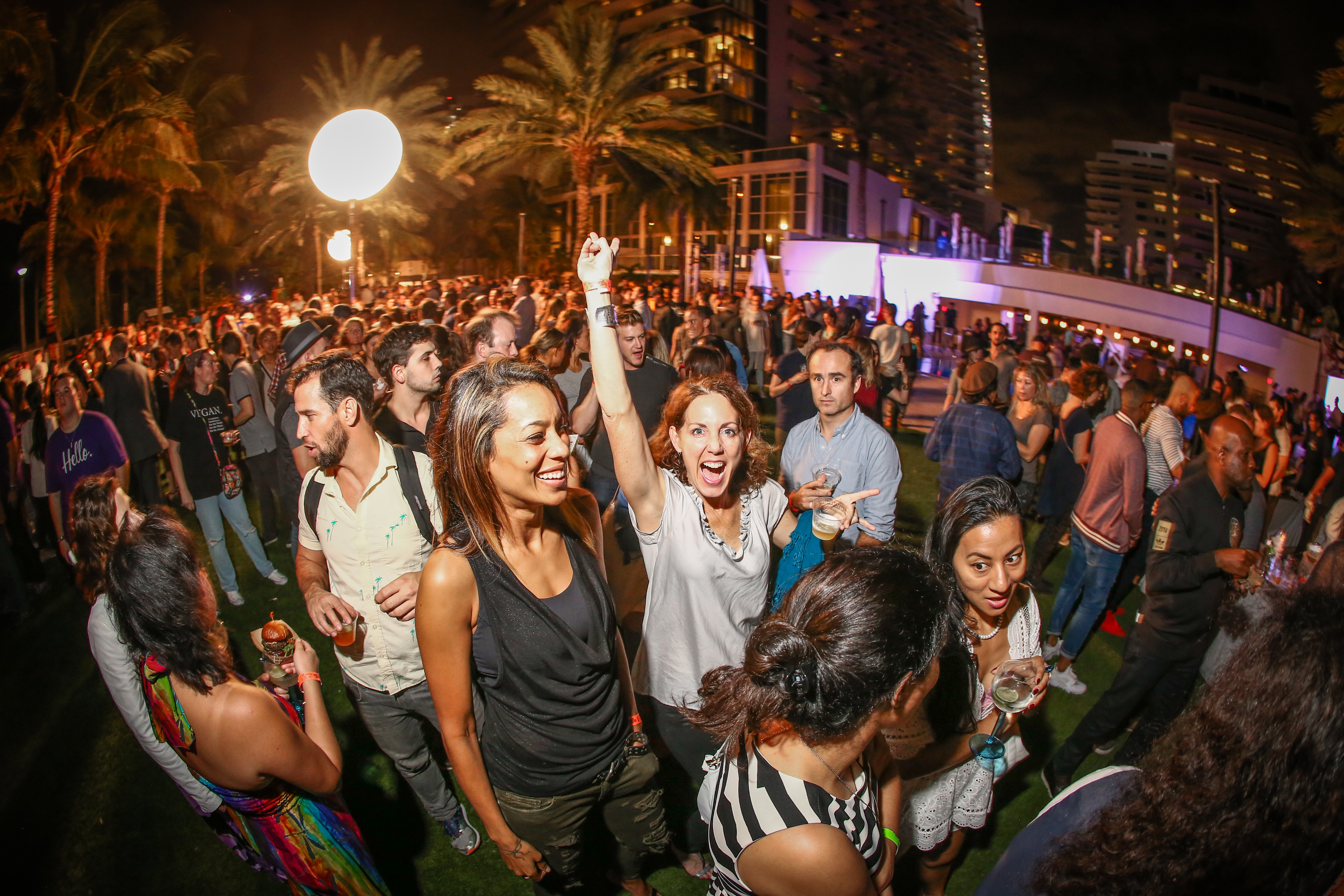 Nighttime outdoor crowd, a woman celebrating with her arm raised under palm trees