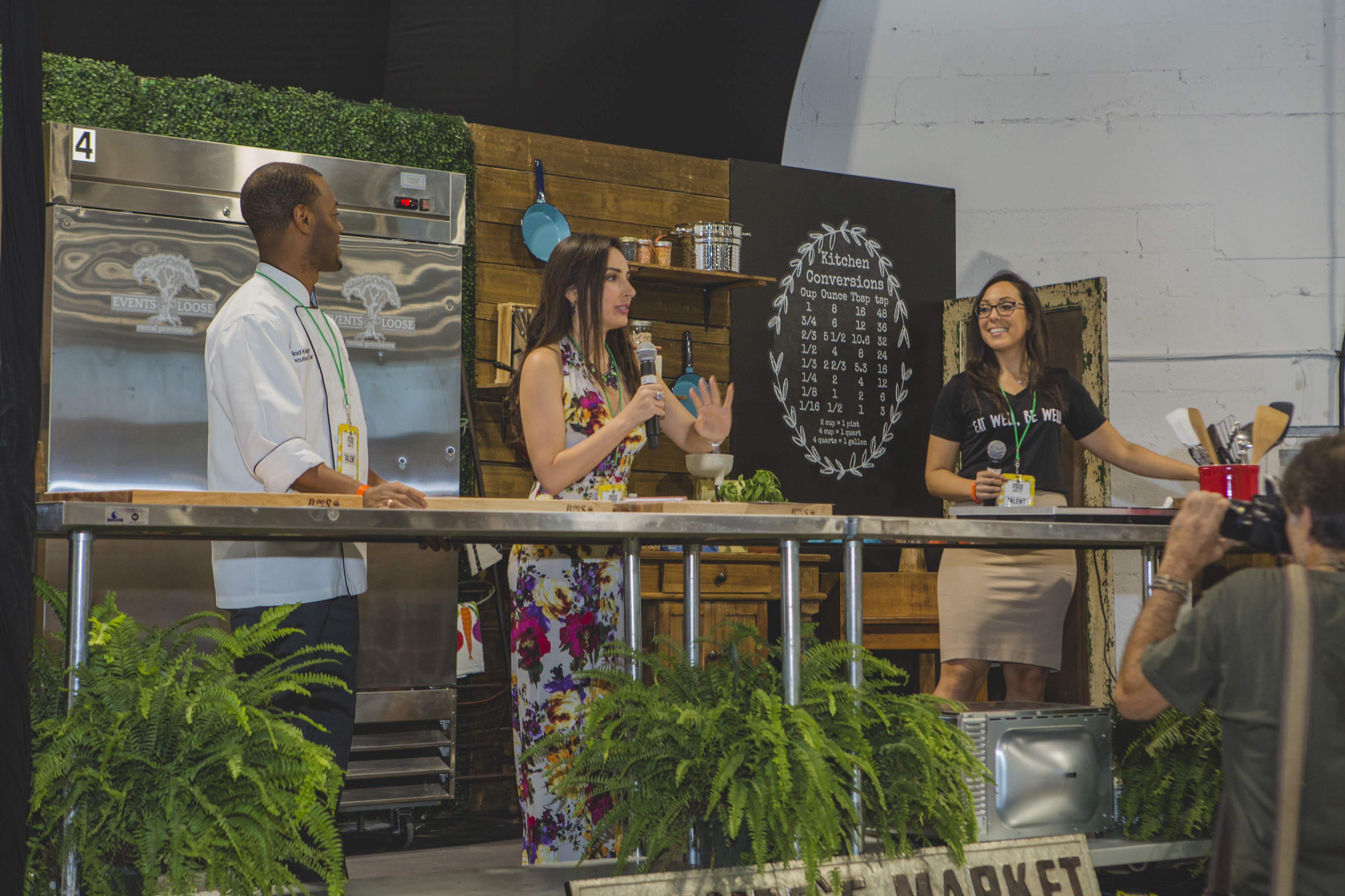 A chef and two presenters on a cooking-demonstration stage