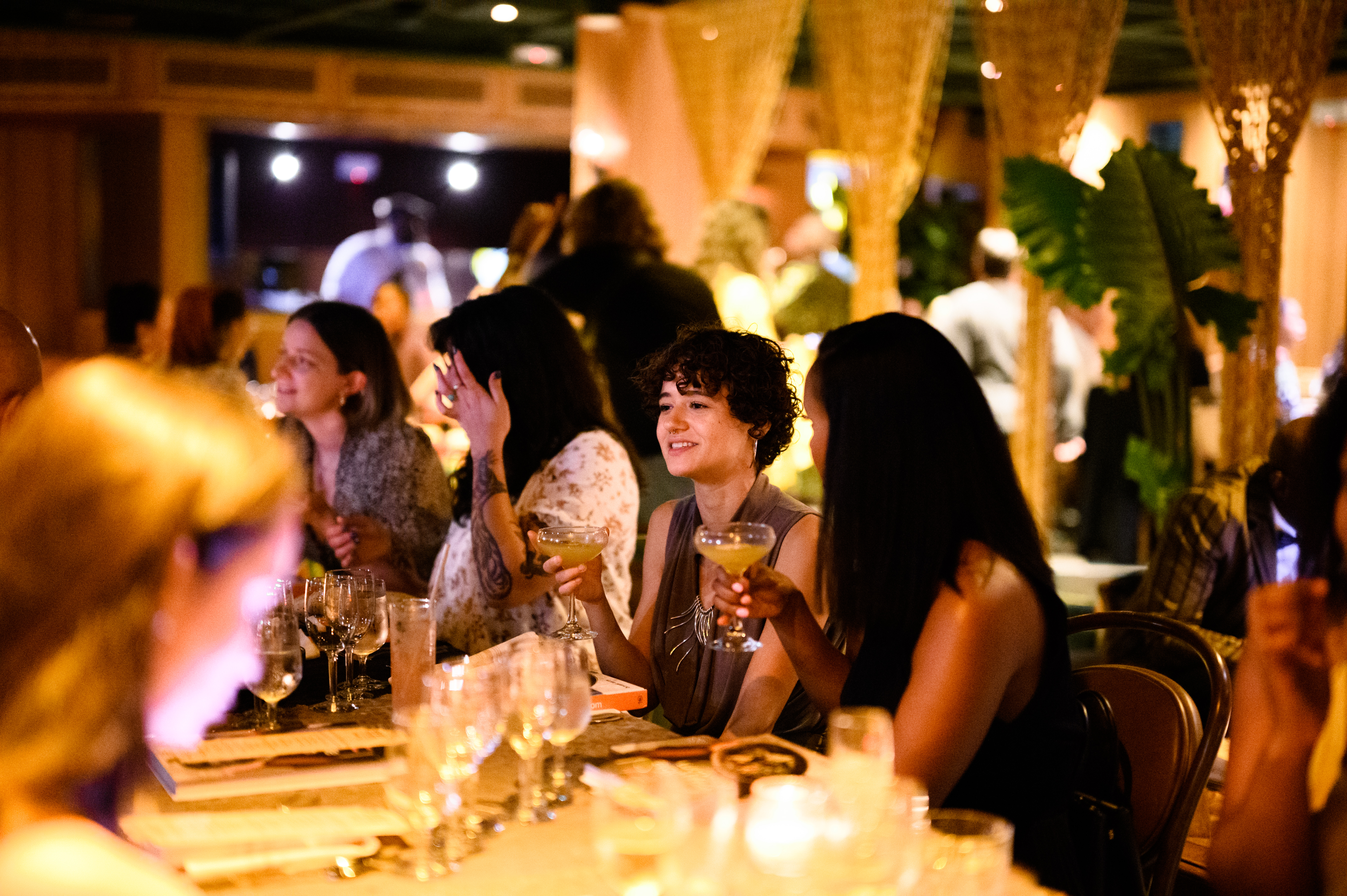 Guests dining at a candlelit table, women toasting with cocktails