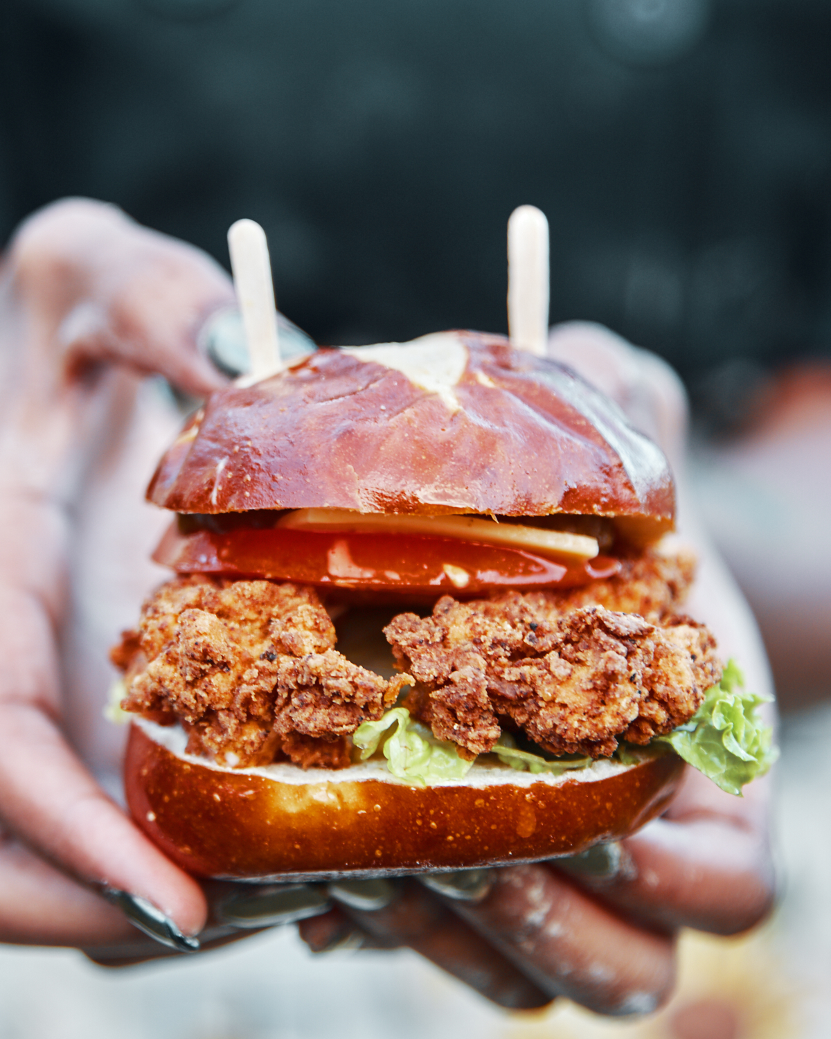 Hands holding a crispy fried vegan slider on a pretzel bun