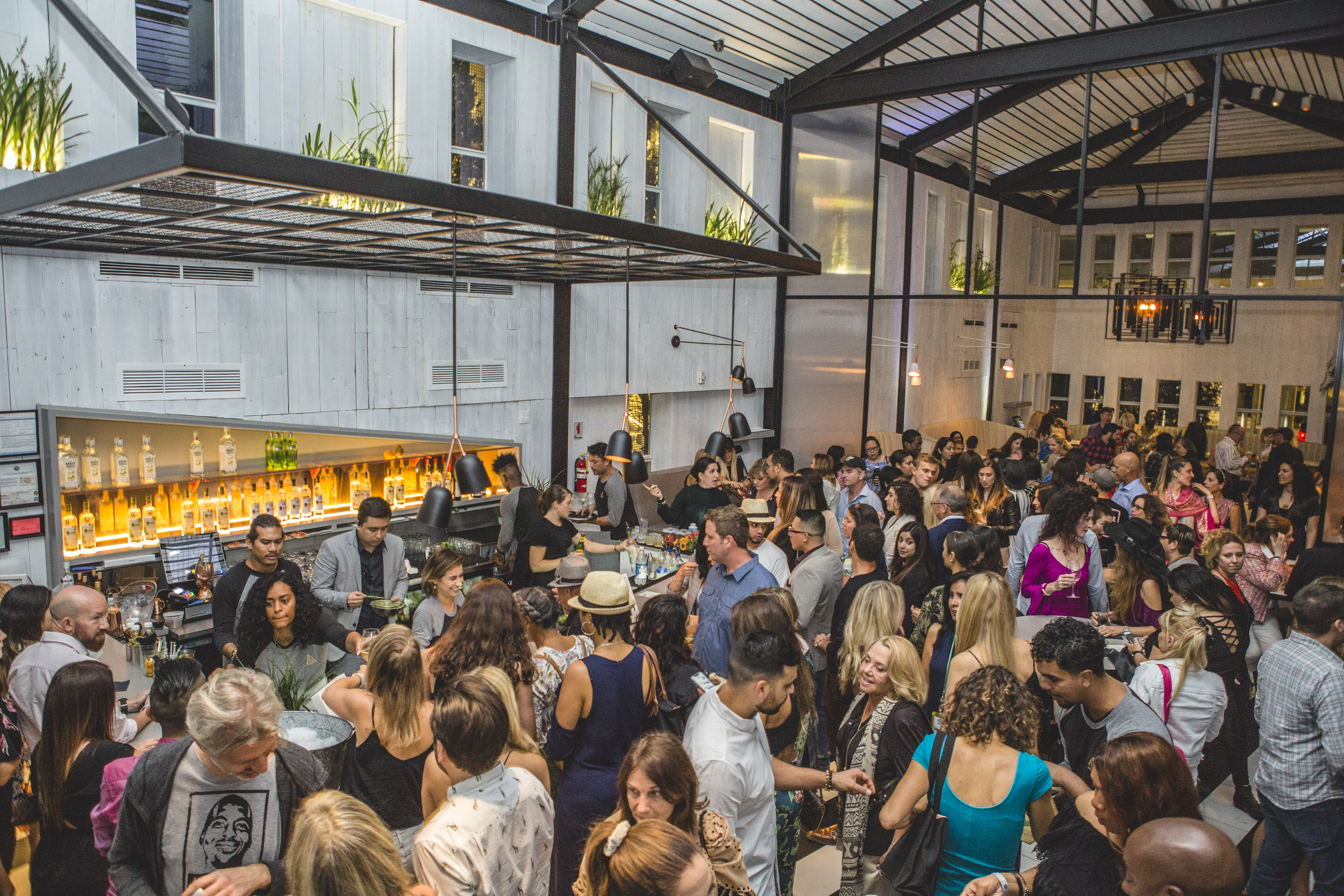 Crowd of attendees mingling at an indoor-outdoor bar venue