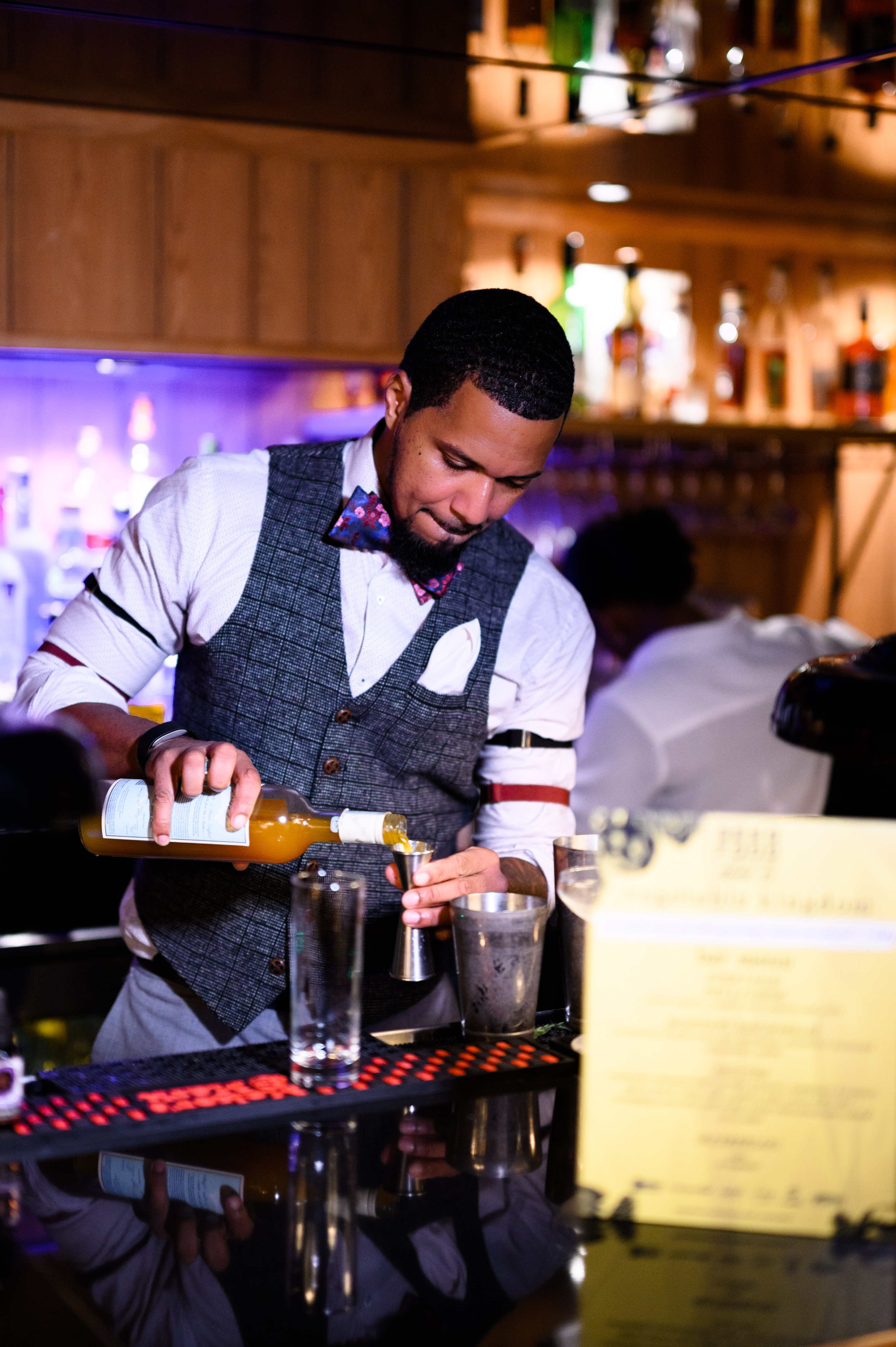Bartender in vest and bow tie pouring spirits into a jigger