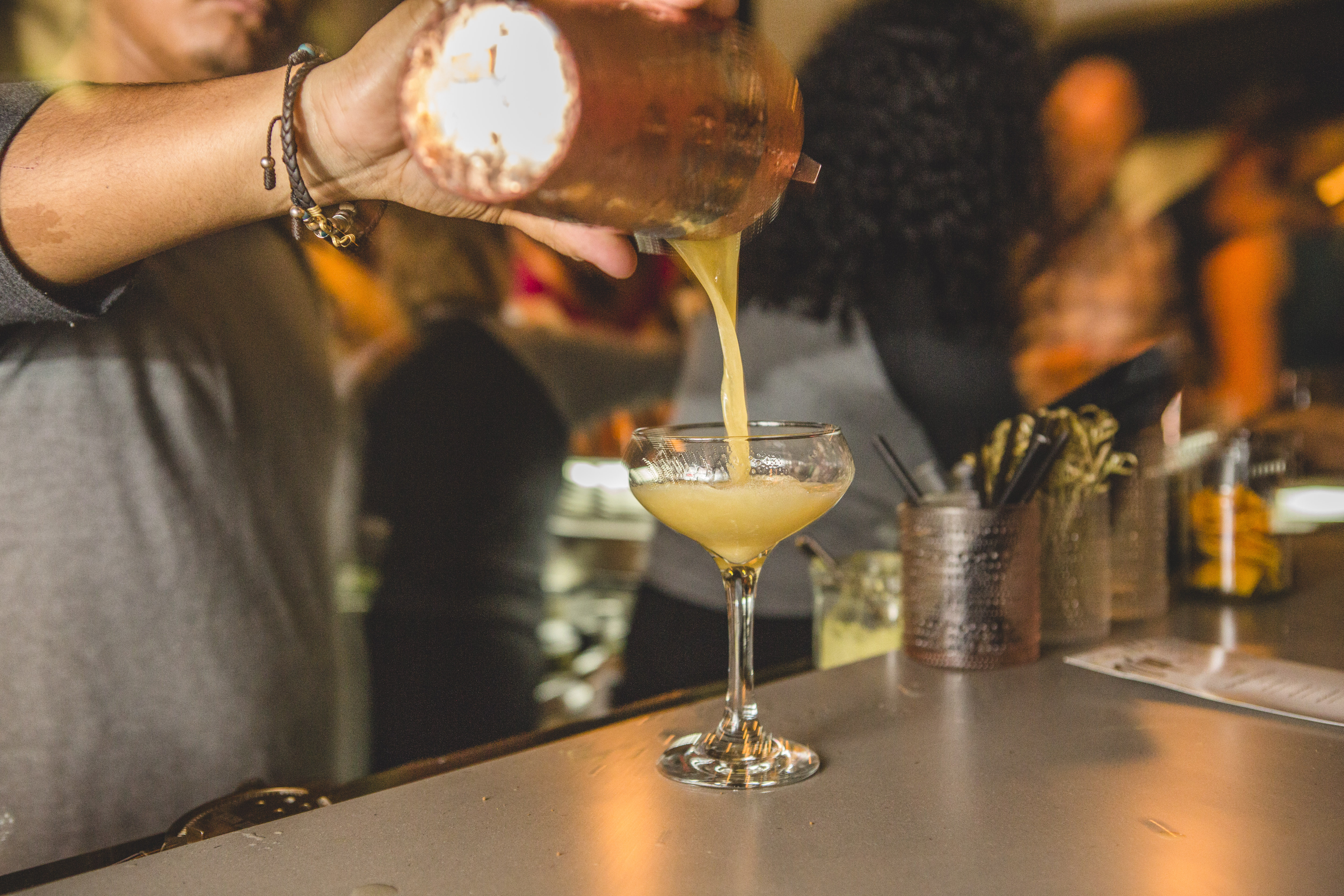 Bartender pouring a cocktail from a copper shaker into a coupe glass