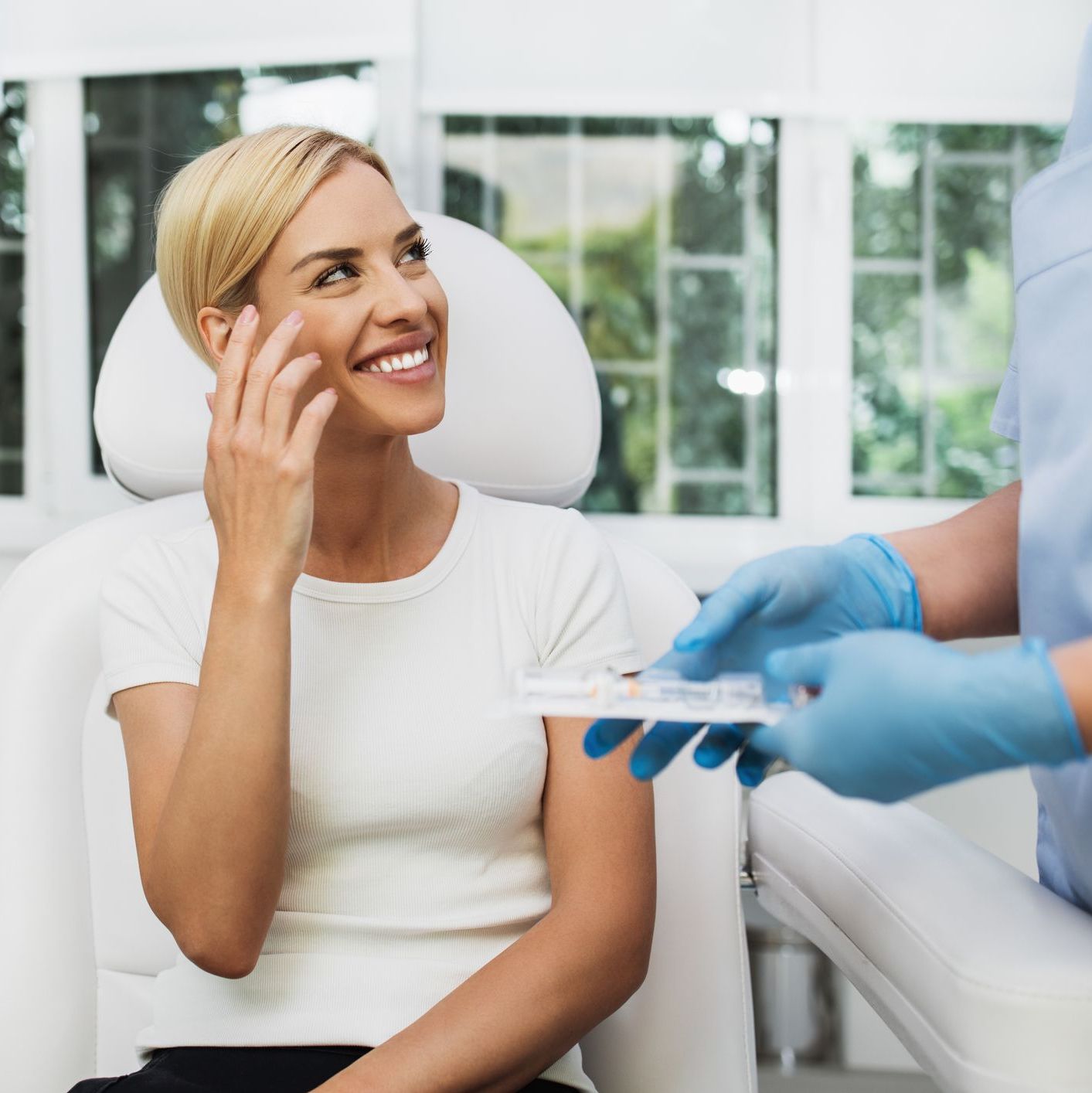 Smiling woman in a treatment chair consulting with a gloved medical provider