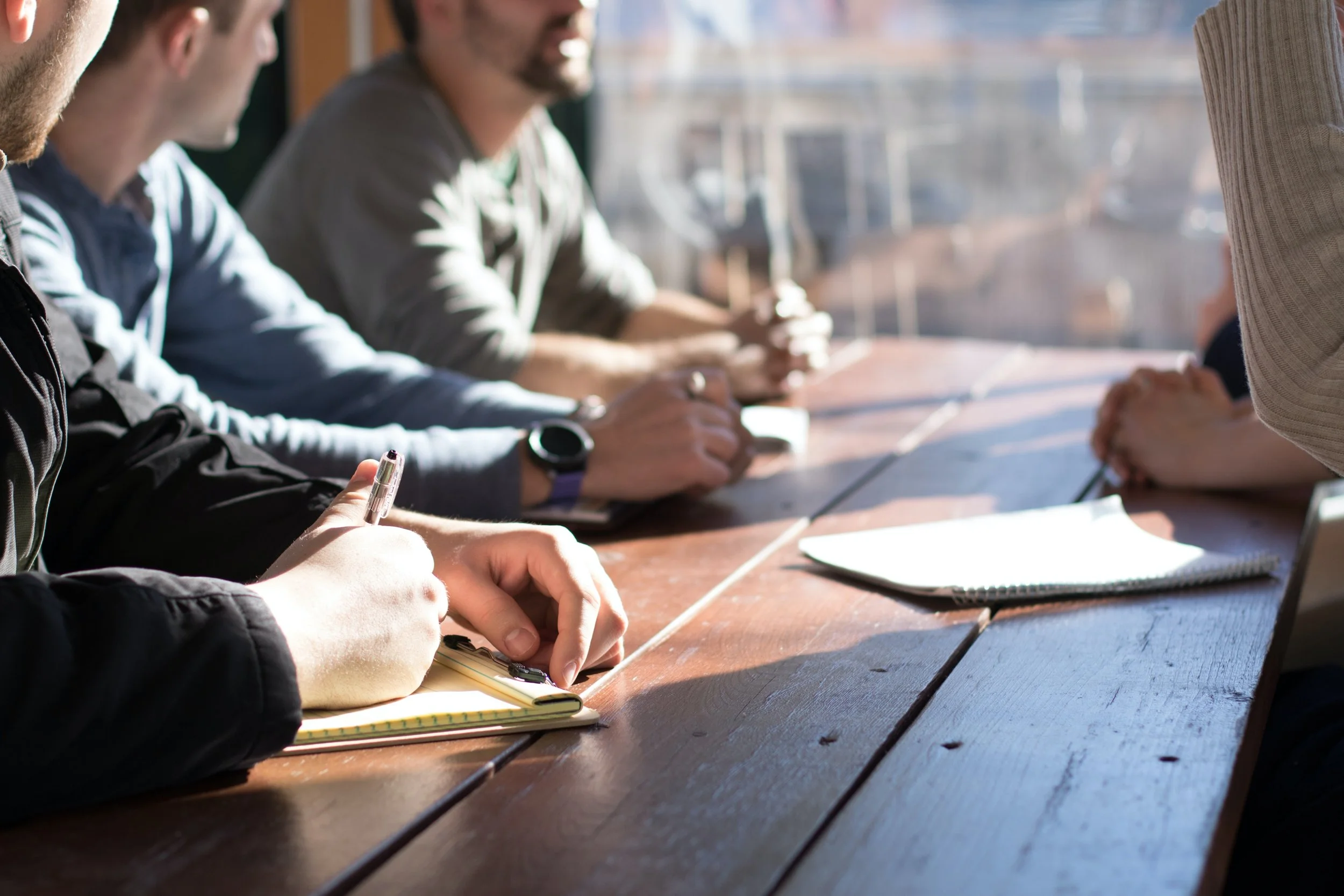 People sitting at a wooden table having a meeting, taking notes in notebooks