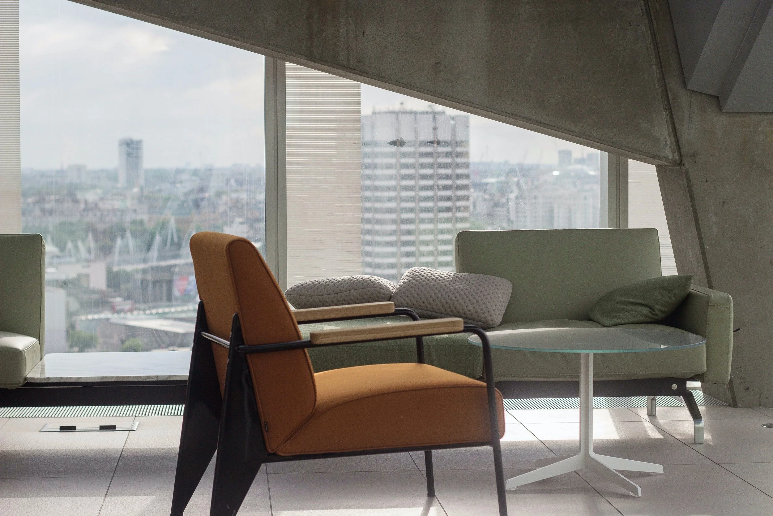 Modern interior with armchair, sofa, and glass coffee table in front of large window with city view