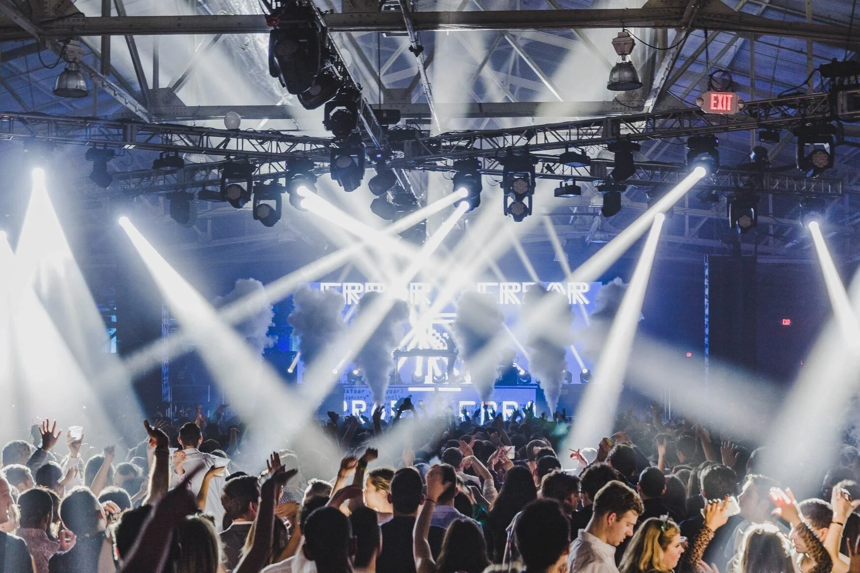 Large crowd dancing inside the main stage with white beam lights