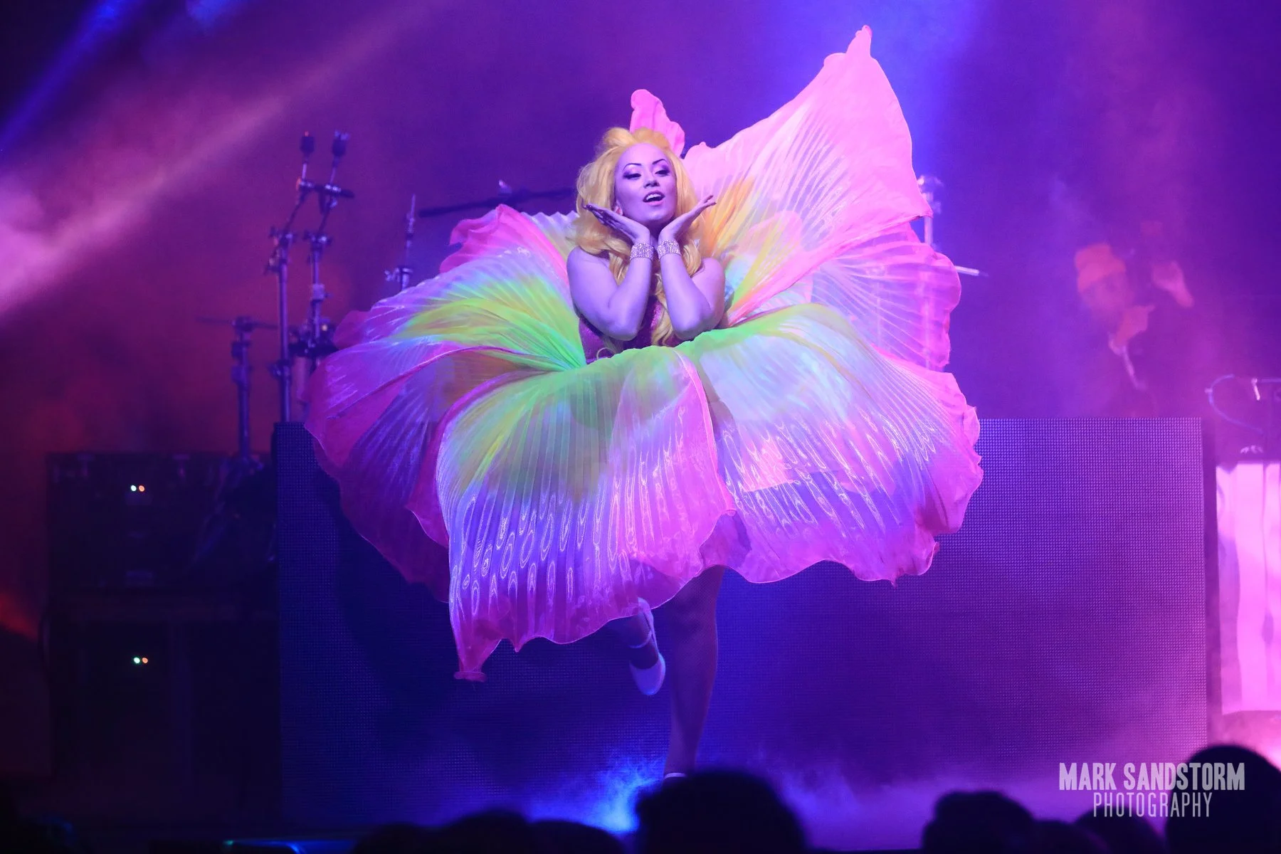 Performer in a large winged costume on stage under purple lighting