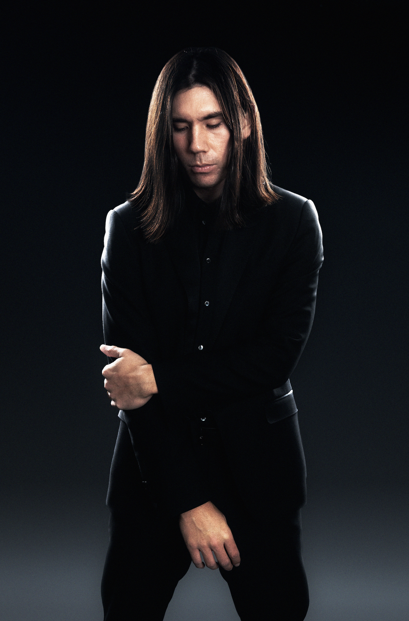 Gryffin press portrait — long-haired artist in a black suit against a dark background