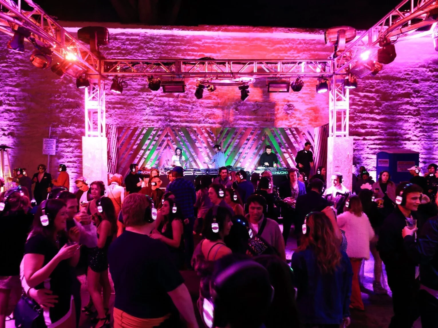 Silent disco crowd wearing wireless headphones under pink and purple lighting
