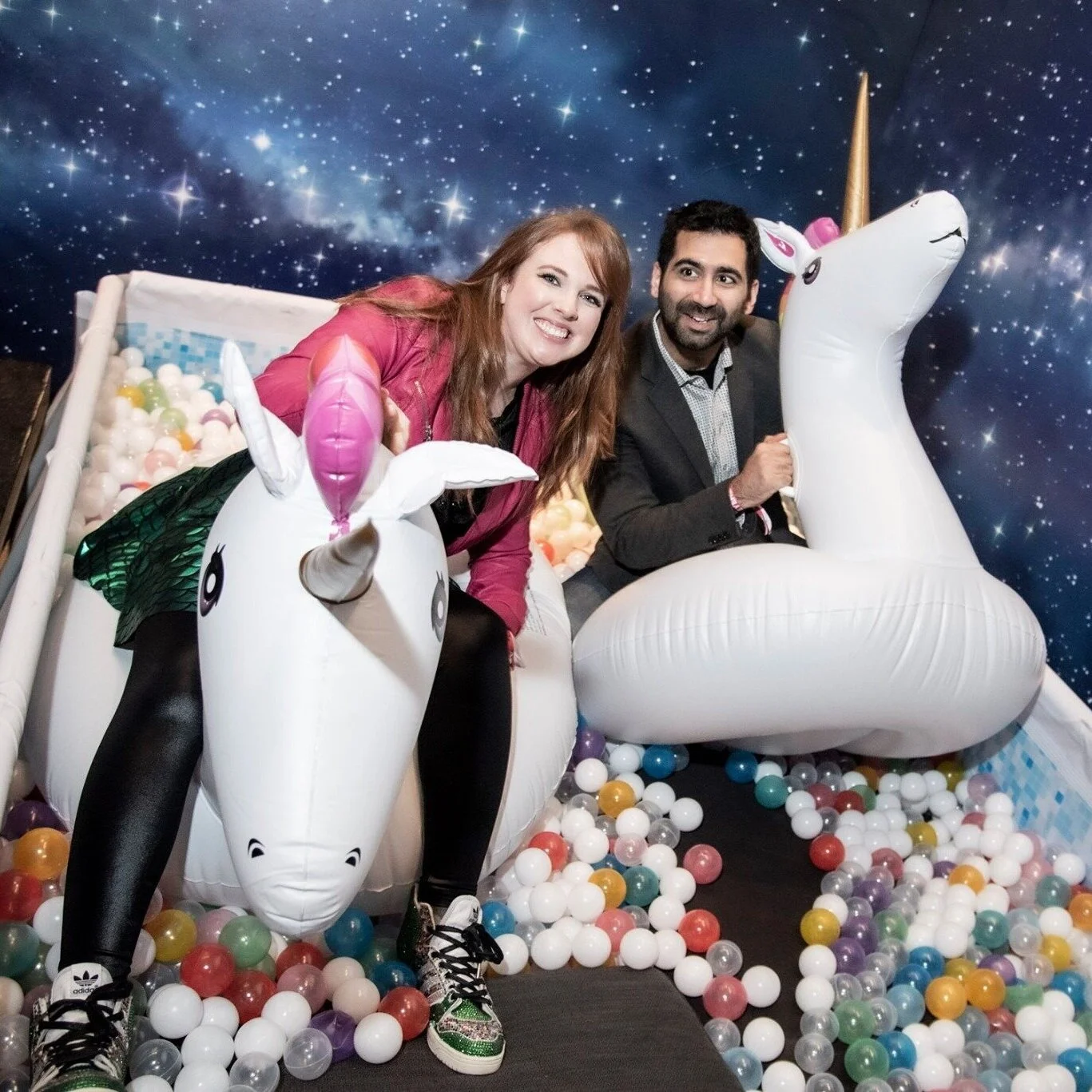 Partygoers with inflatable unicorns in a ball pit with a galaxy backdrop