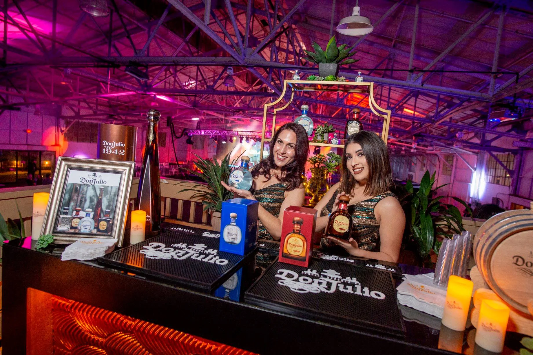 Two women behind a Don Julio bar setup in a purple-lit venue