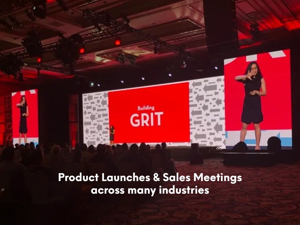 Corporate sales meeting with a speaker on stage flanked by red 'Building GRIT' LED walls