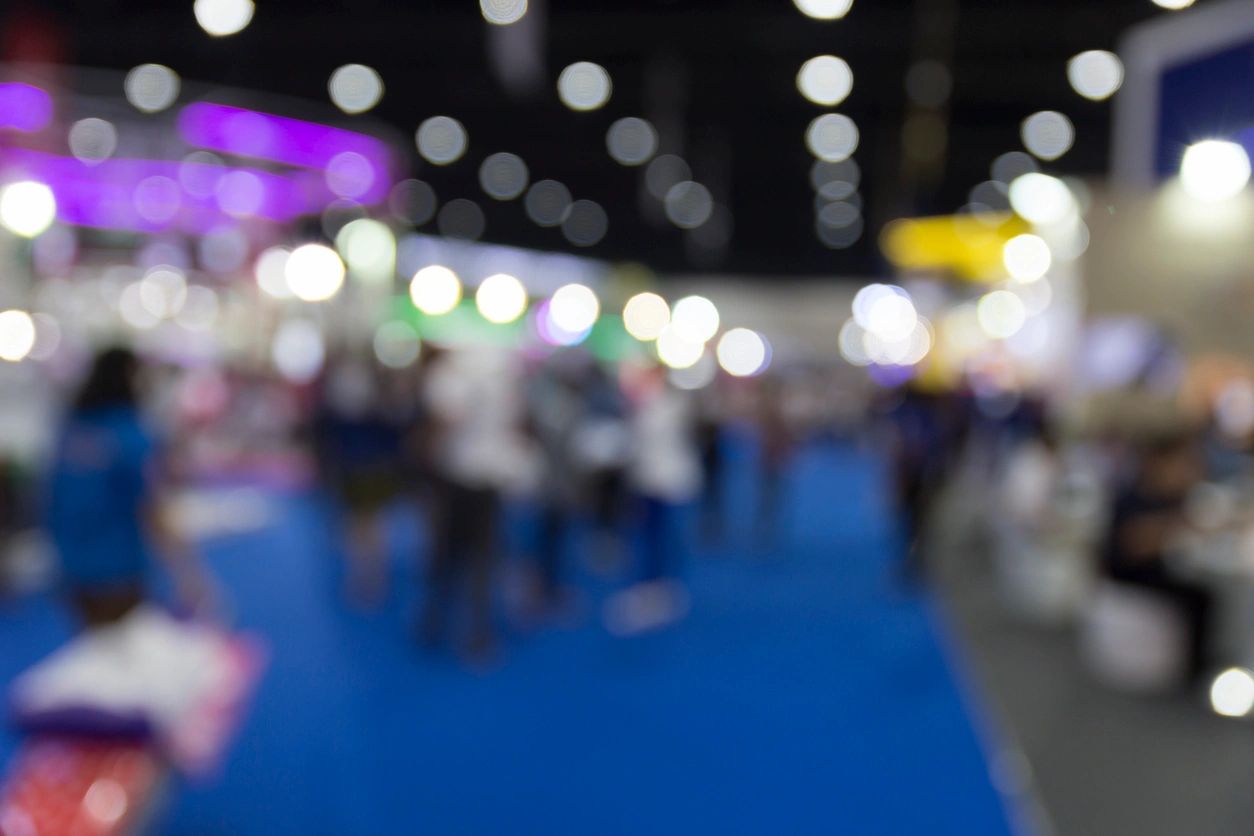 Busy expo and trade-show floor with blue carpet and colorful lights