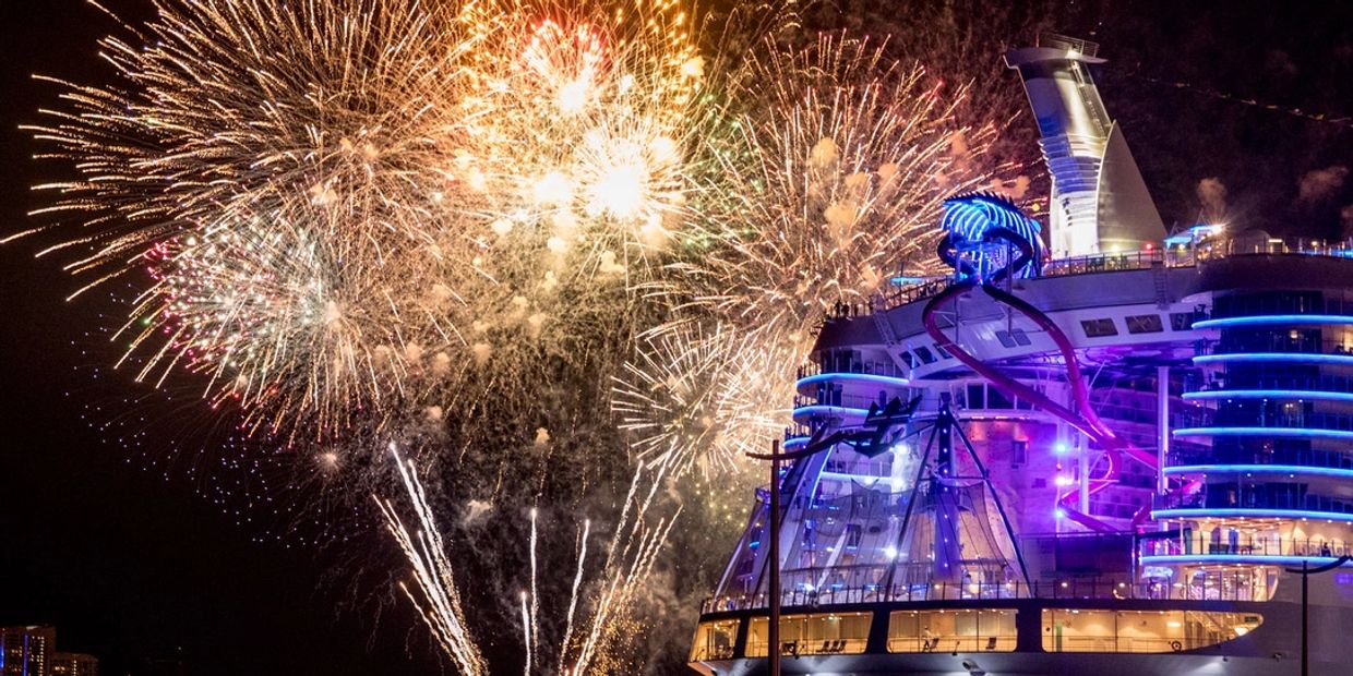 Fireworks bursting over an illuminated cruise ship at night