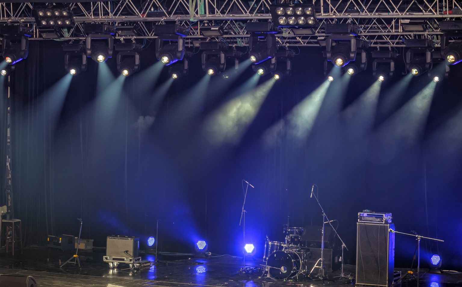 Empty concert stage lit in blue with drum kit and rigging truss