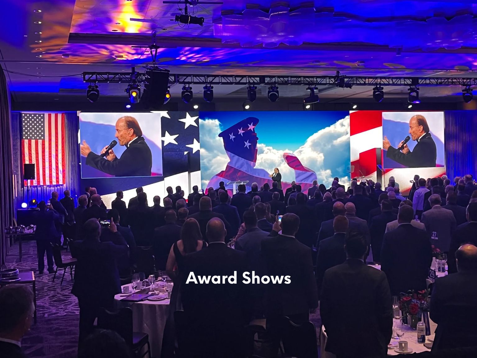 Ballroom award show with LED screens showing a speaker and flag imagery