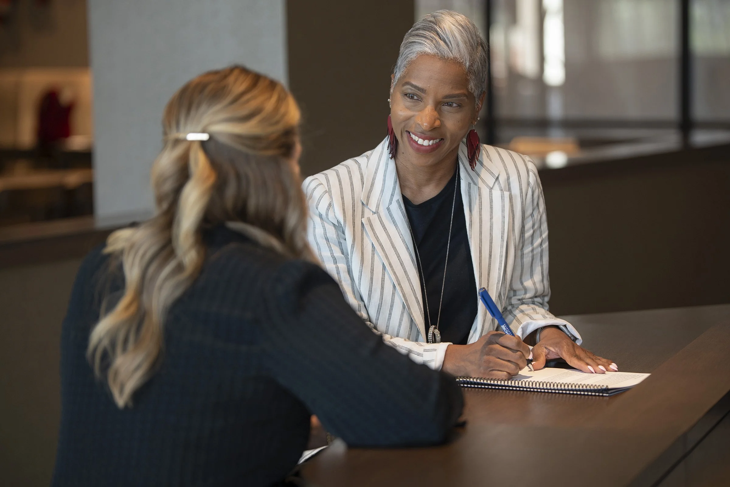 Two people meeting across a table, one writing in a notebook during a coaching conversation