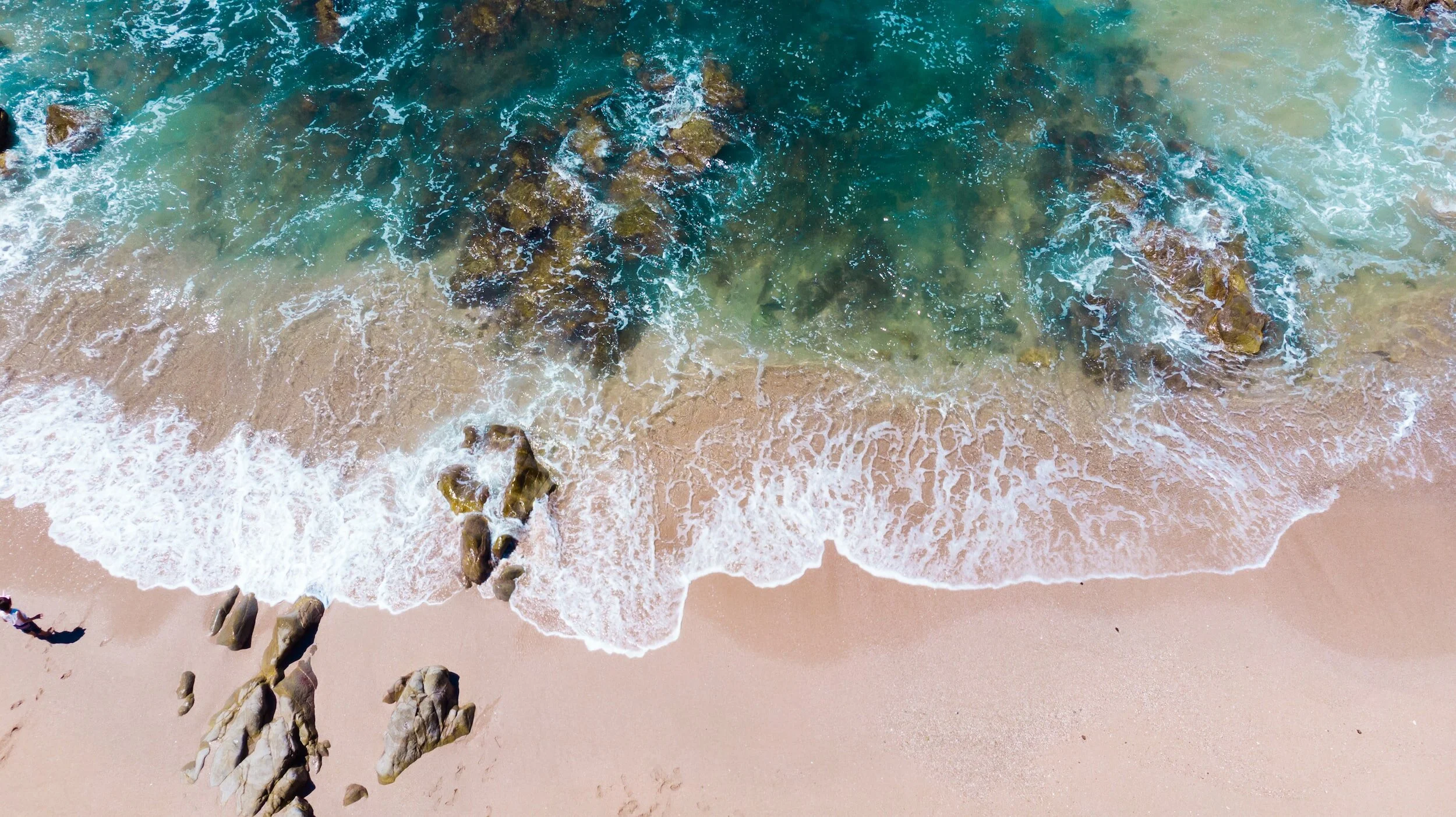 Aerial view of ocean waves washing onto a sandy beach with rocky outcrops