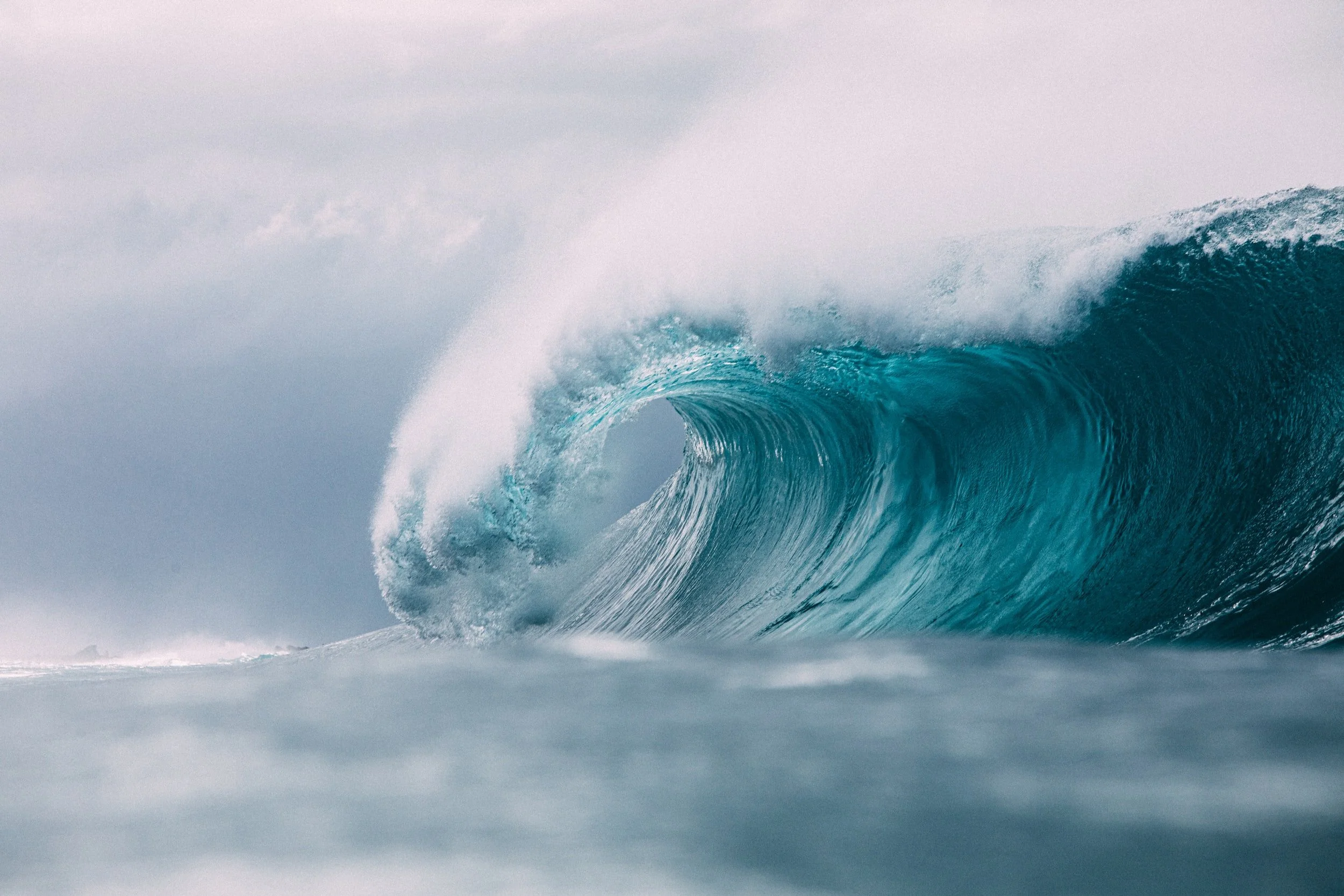 A large ocean wave curling over itself under an overcast sky