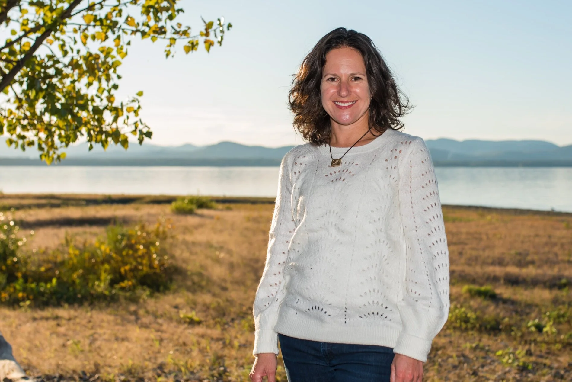 Erika Schram, founder of Skylight Coaching & Consulting, standing by a lake with mountains behind her