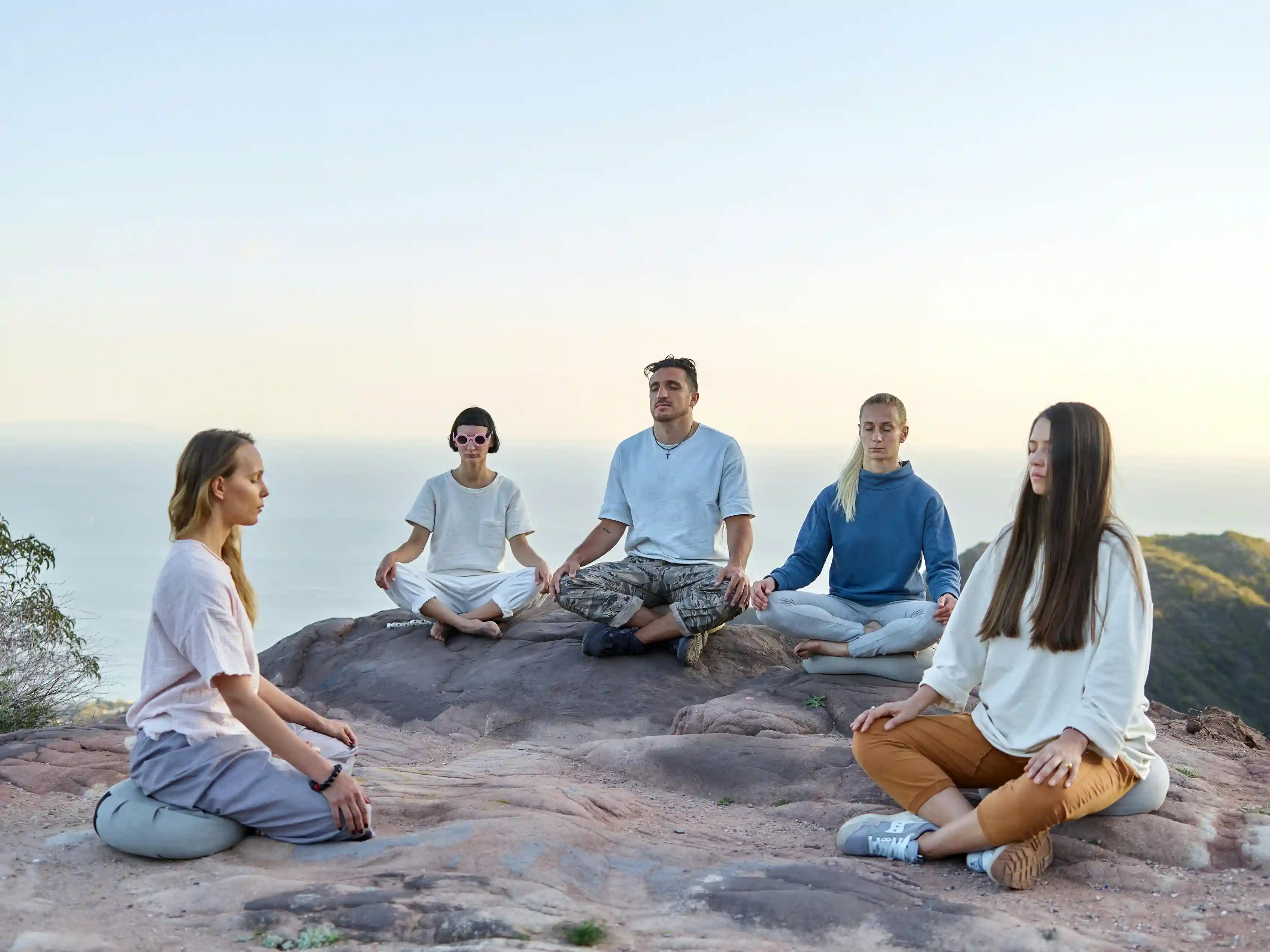 Group meditating on a rocky hilltop overlooking the sea
