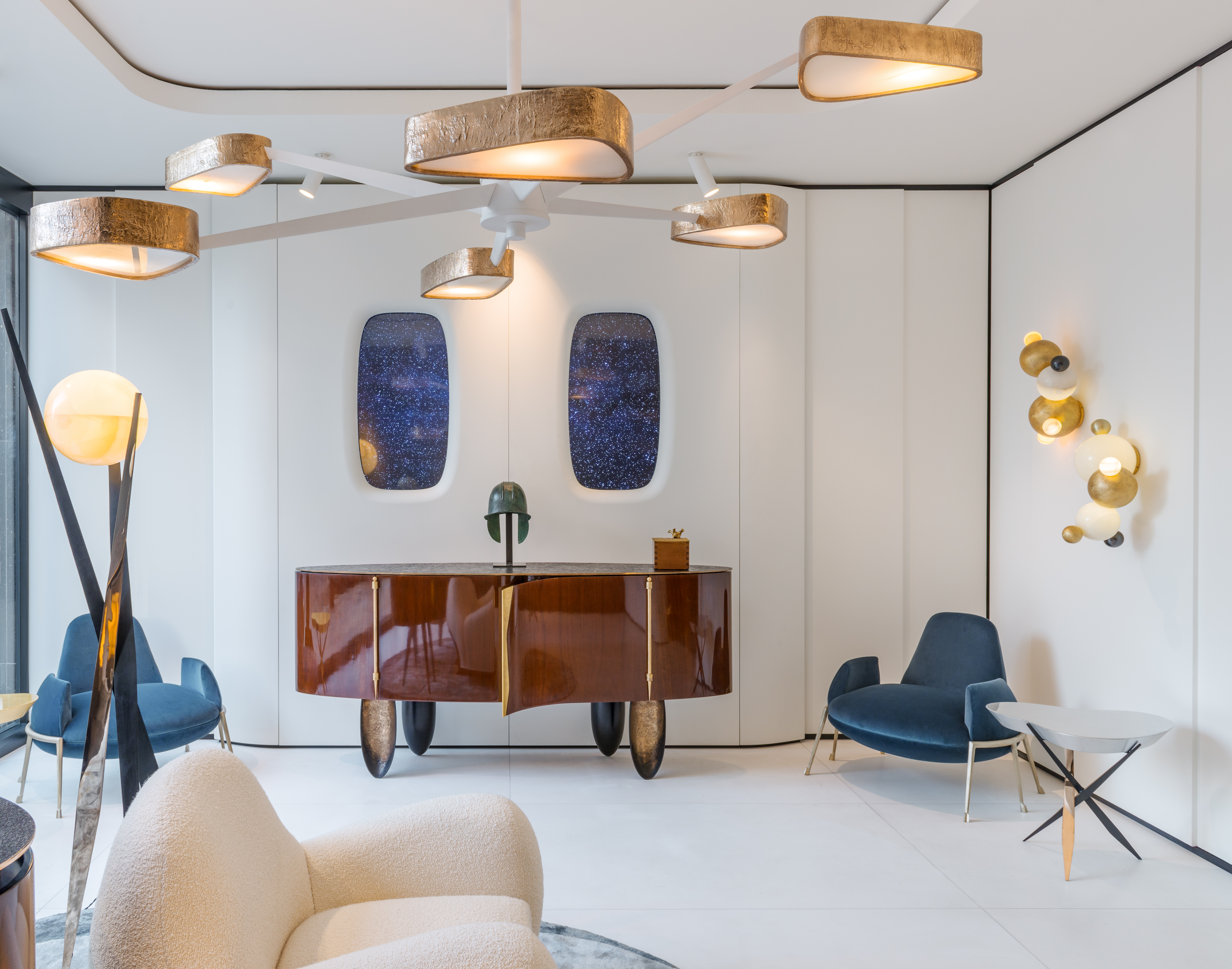 Contemporary showroom with gold-leaf ceiling fans, blue velvet chairs, sculptural credenza and galaxy-print wall panels