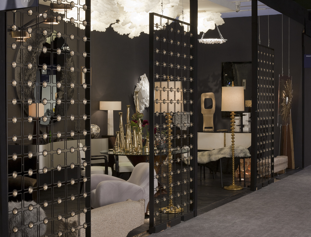 Dark trade-show display with black metal grid partitions holding crystal orbs, a cloud light fixture and luxe furniture