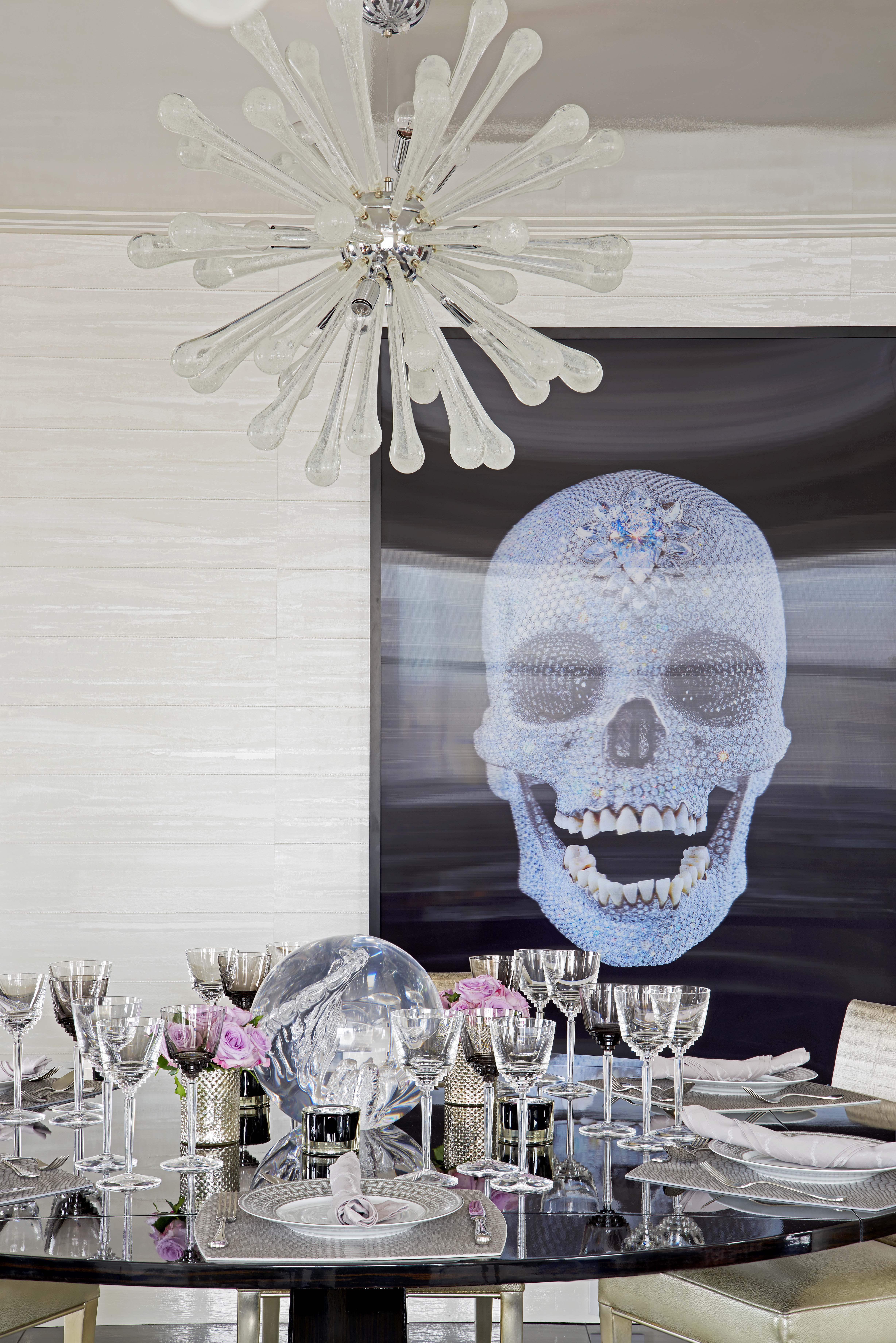 Glamorous dining room with a crystal sputnik chandelier, jeweled skull artwork and an elegantly set black glass table