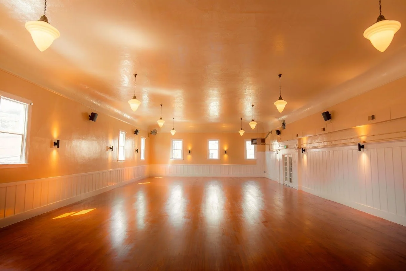 The Castro Room event hall in San Francisco with polished hardwood floor, pendant lights and warm orange walls