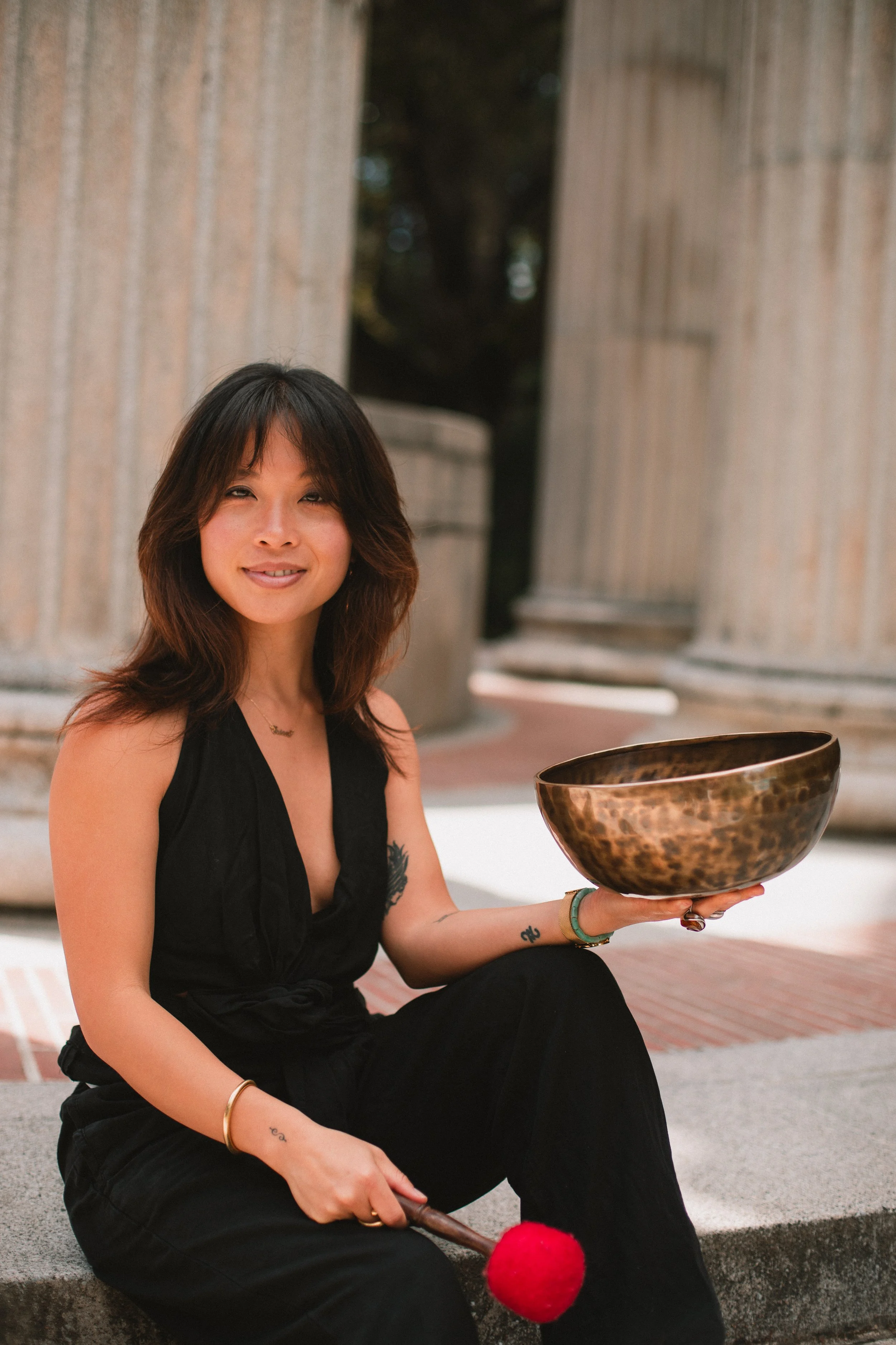 Erica Nguyễn seated on stone steps holding a Tibetan singing bowl and mallet