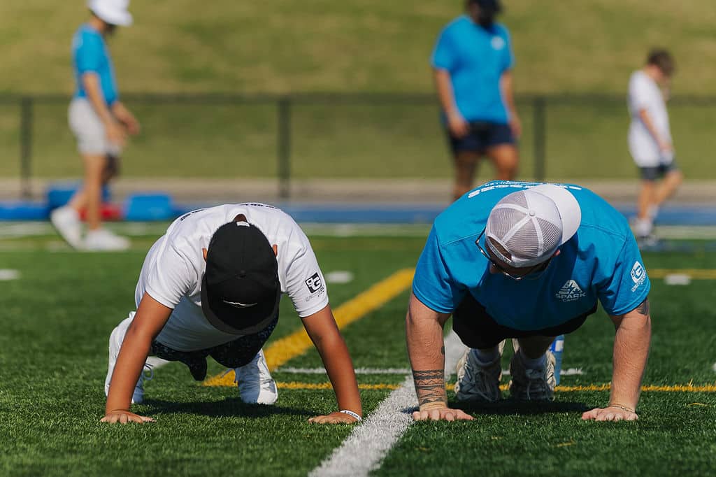 Camper and coach doing push-ups on the turf field