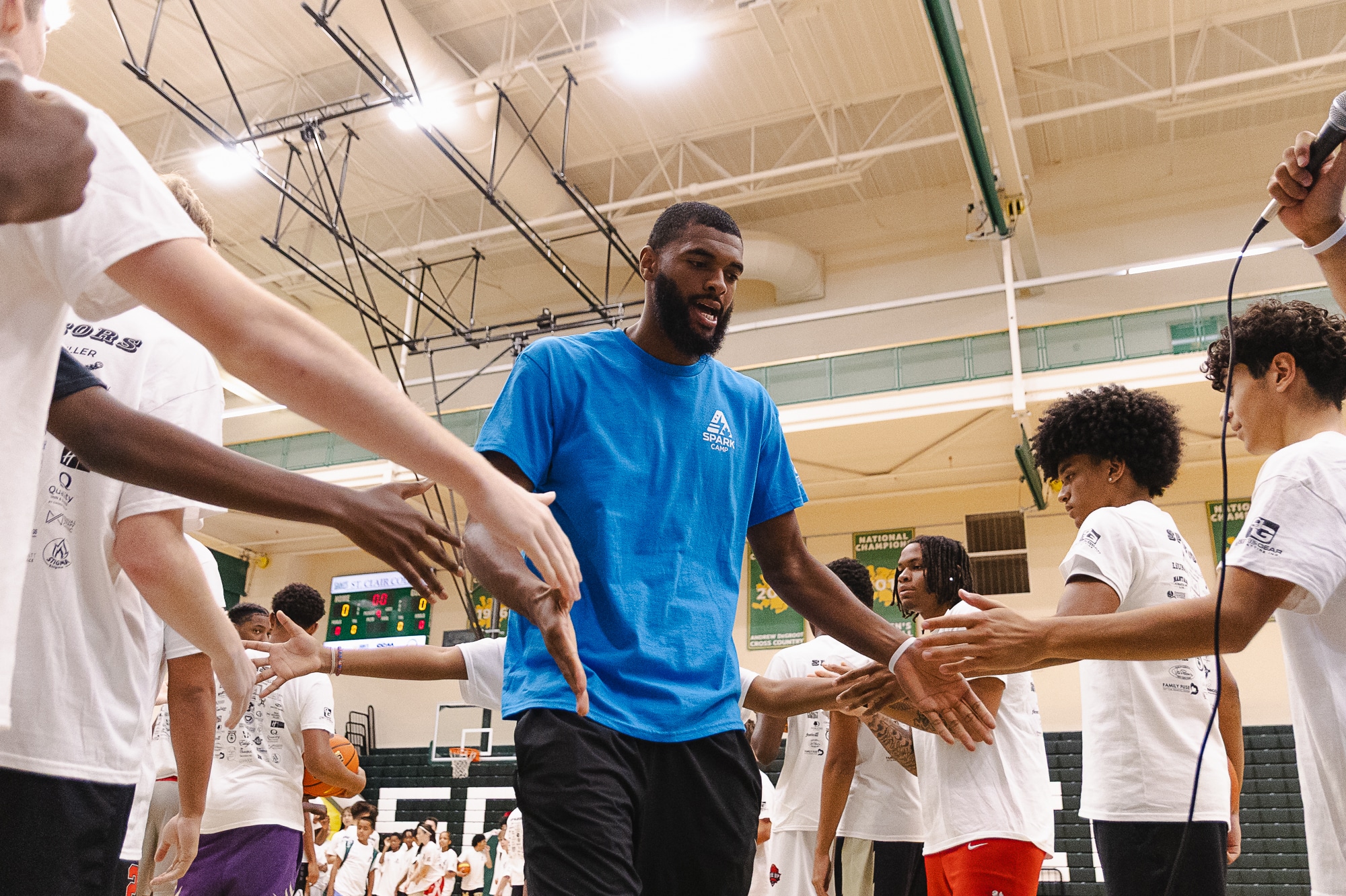 Tall coach high-fiving a line of young campers on the court