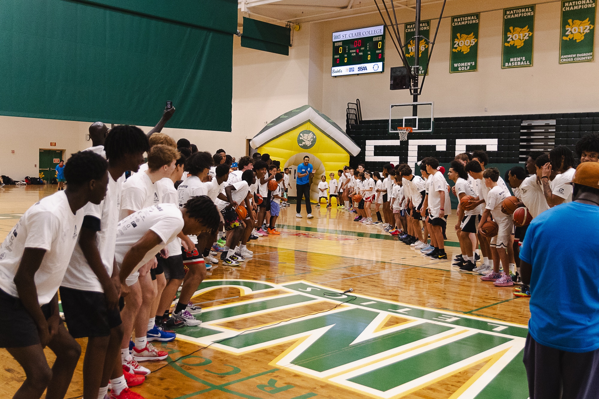 Large group of Spark Camp athletes in white shirts facing a coach at center court at St. Clair College