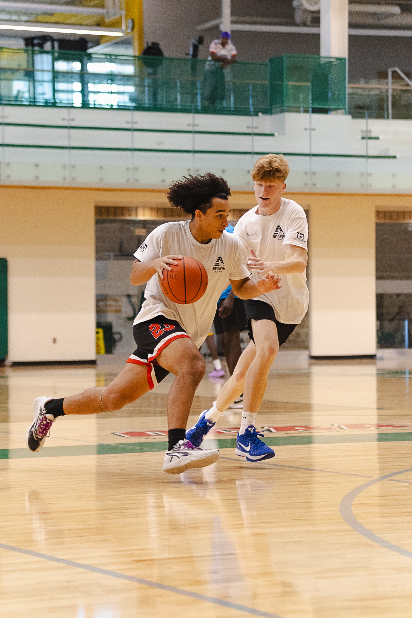 Two teen campers in Spark Camp shirts playing one-on-one basketball