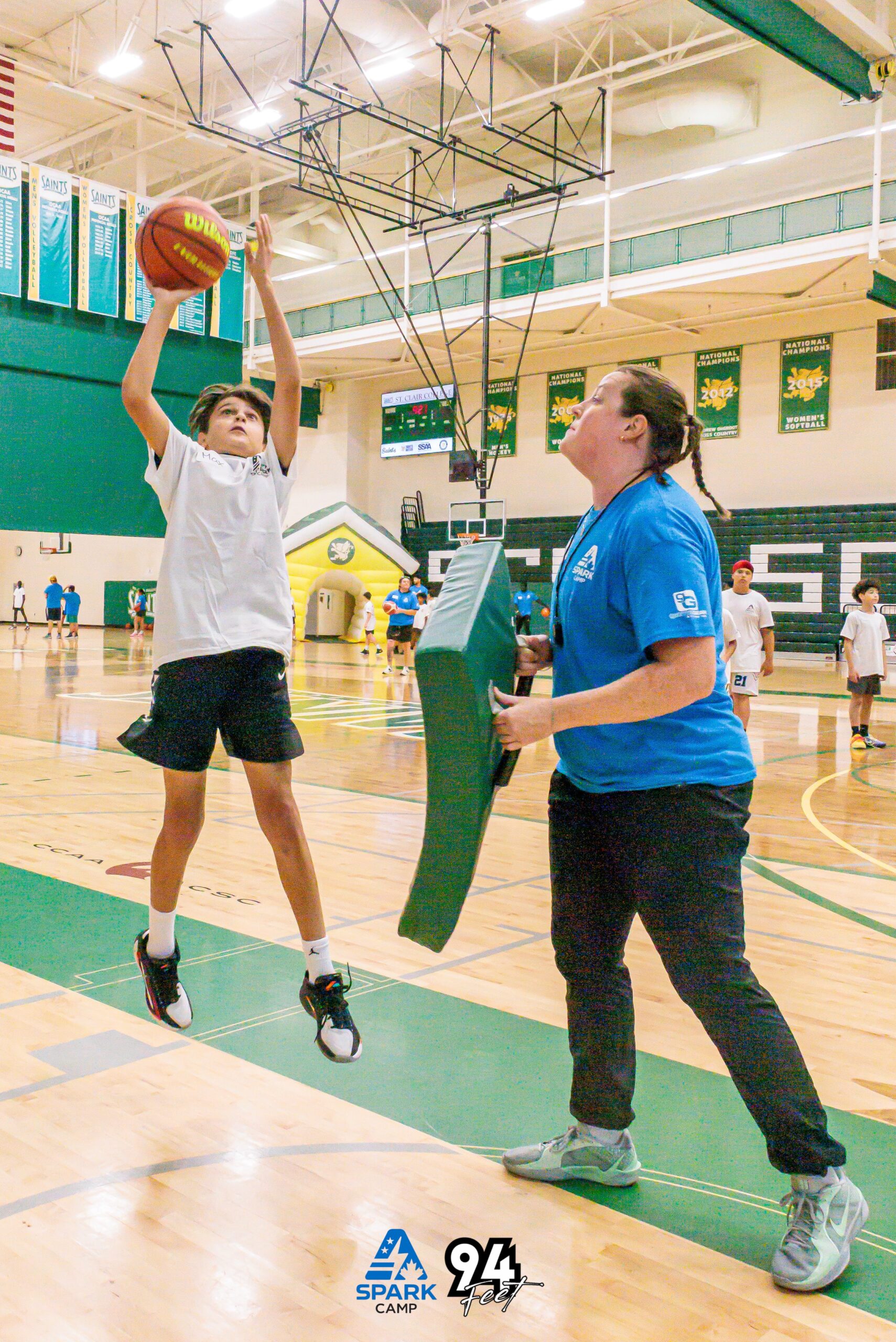 Young camper jumping to shoot while a coach holds a blocking pad